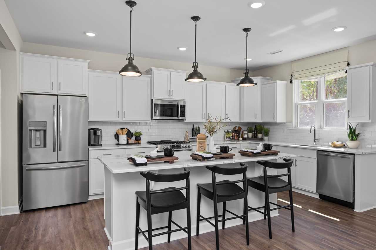 Modern kitchen in Wellers Knoll Lillington NC with white cabinets, stainless steel appliances, center island, black stools, and hardwood floors