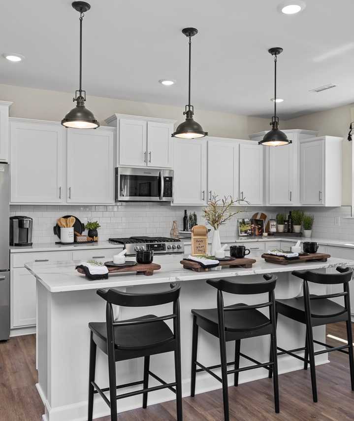 Modern kitchen in Wellers Knoll Lillington NC with white cabinets, stainless steel appliances, island bar, black stools, hardwood floors