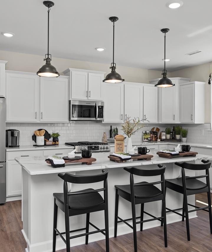 Modern kitchen in Wellers Knoll Lillington NC with white cabinets, stainless steel appliances, island bar, black stools, hardwood floors