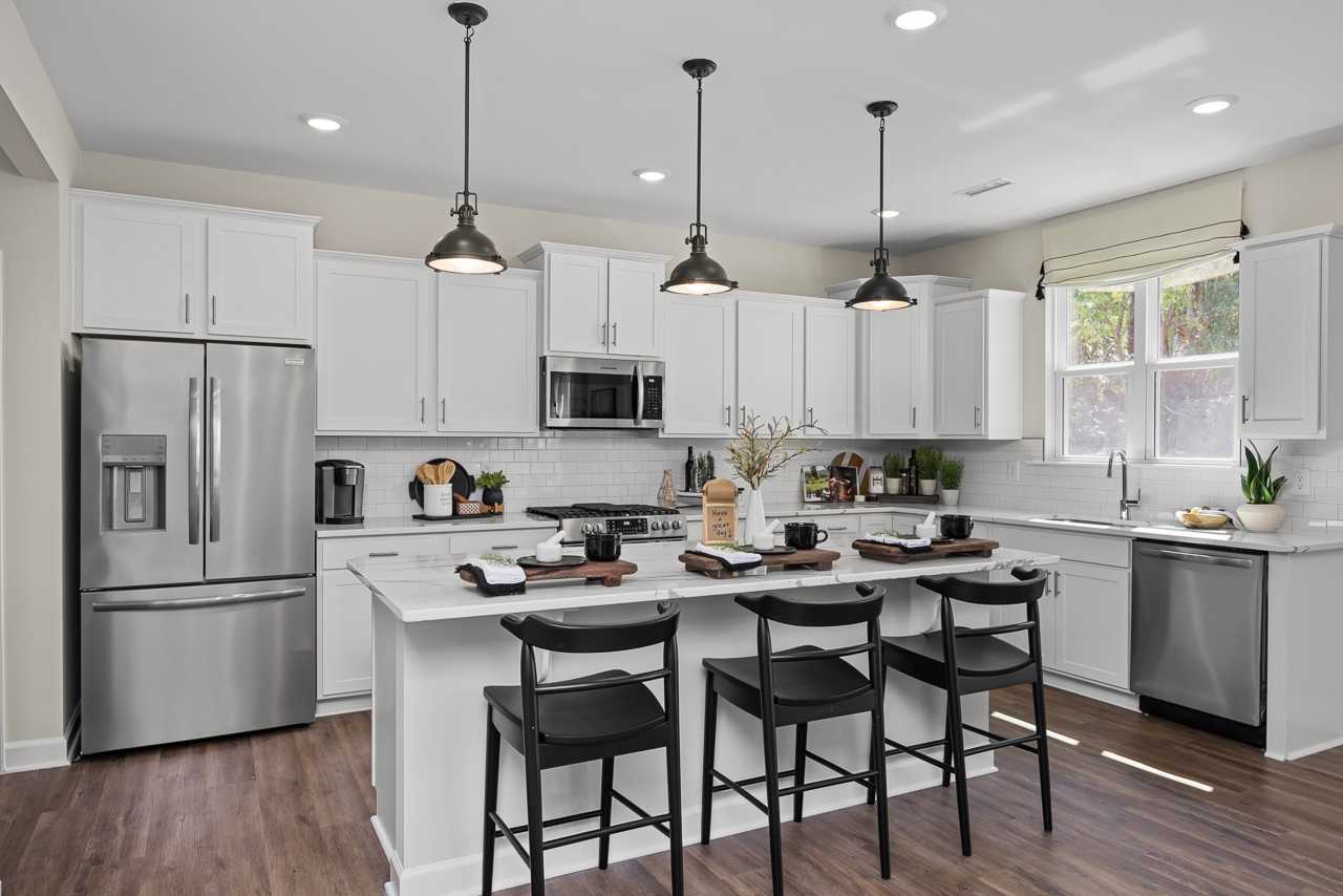 Modern kitchen in Wellers Knoll Lillington NC with white cabinets, stainless steel appliances, island bar, black stools, hardwood floors