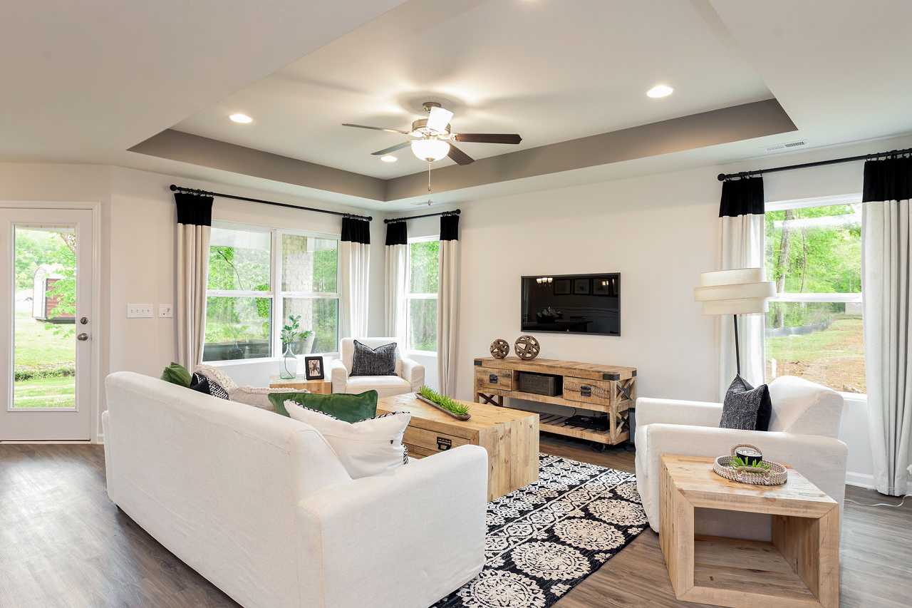 Spacious living room in The Franklin home with white sofas, wooden media console, ceiling fan, large windows, and hardwood floors