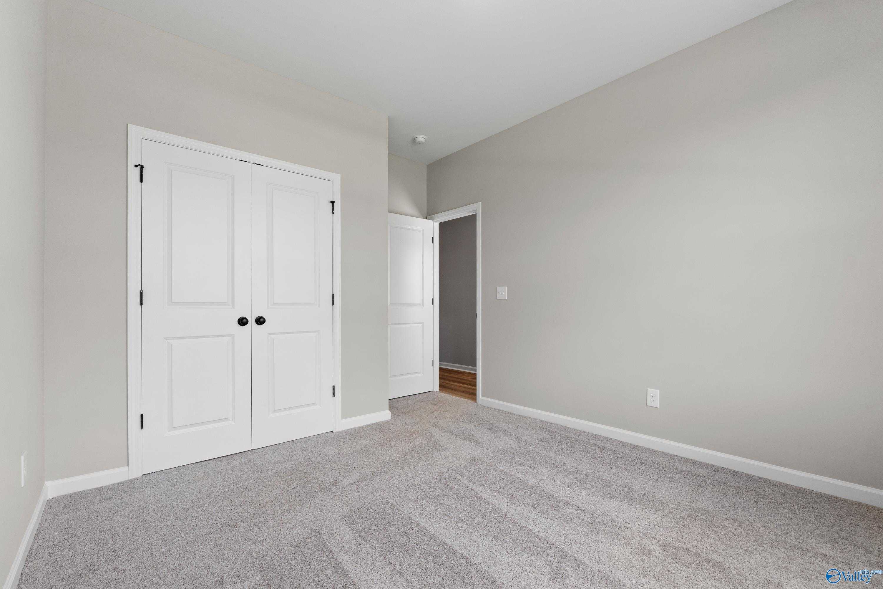 Spacious secondary bedroom with light gray walls, white double closet doors, and beige carpet in Evermore Homes The Nantucket, Madison, Alabama