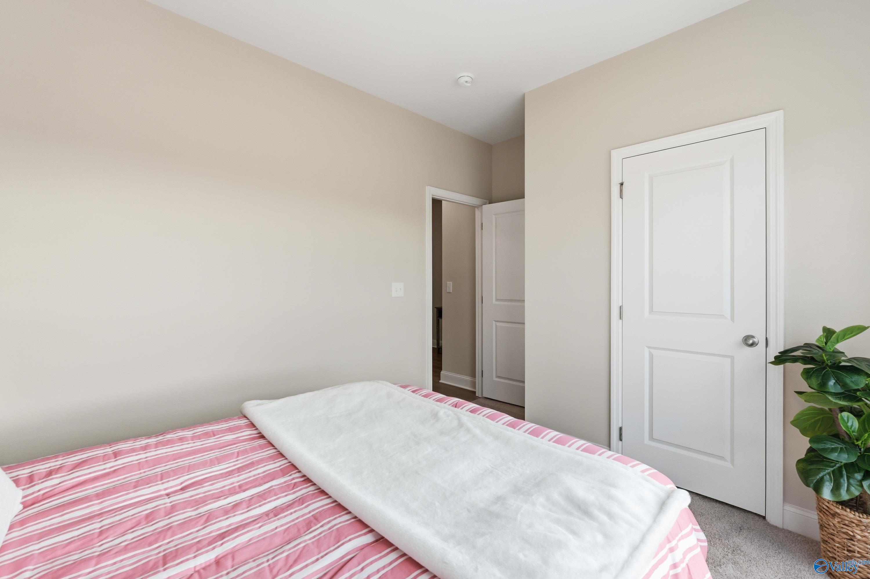 Cozy bedroom with pink striped bedding, white throw blanket, potted plant, and beige walls in Davidson Homes The Asheville, Toney, Alabama