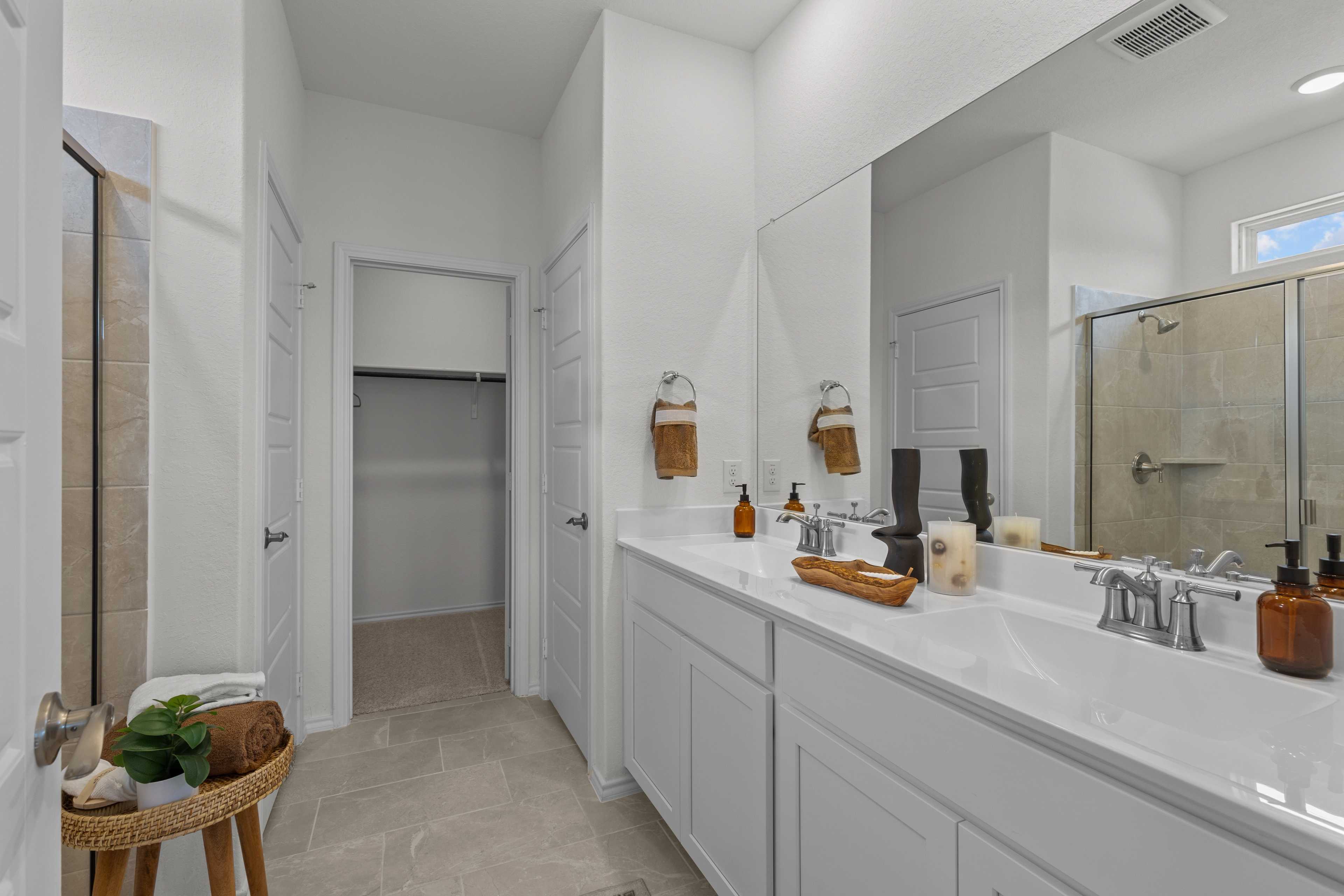 Spacious master bathroom in The Daphne H featuring white double vanity, glass walk-in shower, and closet by Davidson Homes