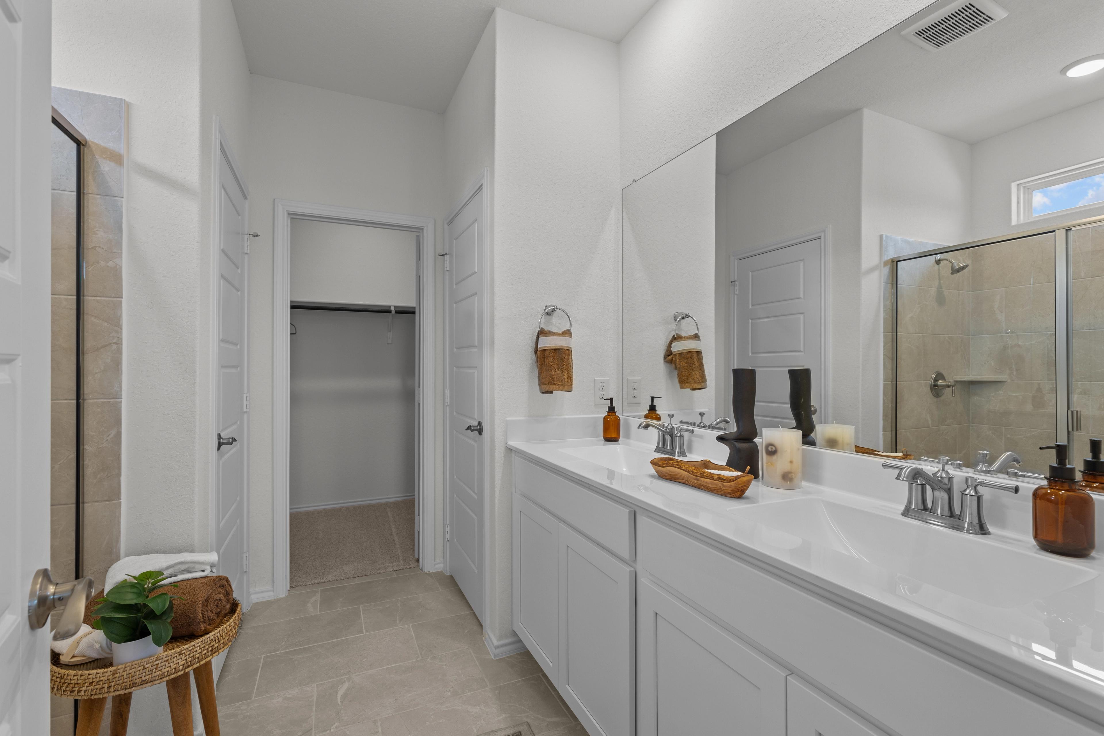 Spacious master bathroom in The Daphne G featuring white double vanity, glass walk-in shower, and adjacent closet