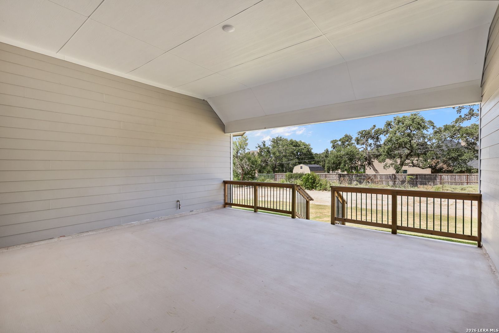 Covered back patio with wooden railing overlooking the backyard in The Summerlin B home, Potranco Oaks, Castroville, Texas.