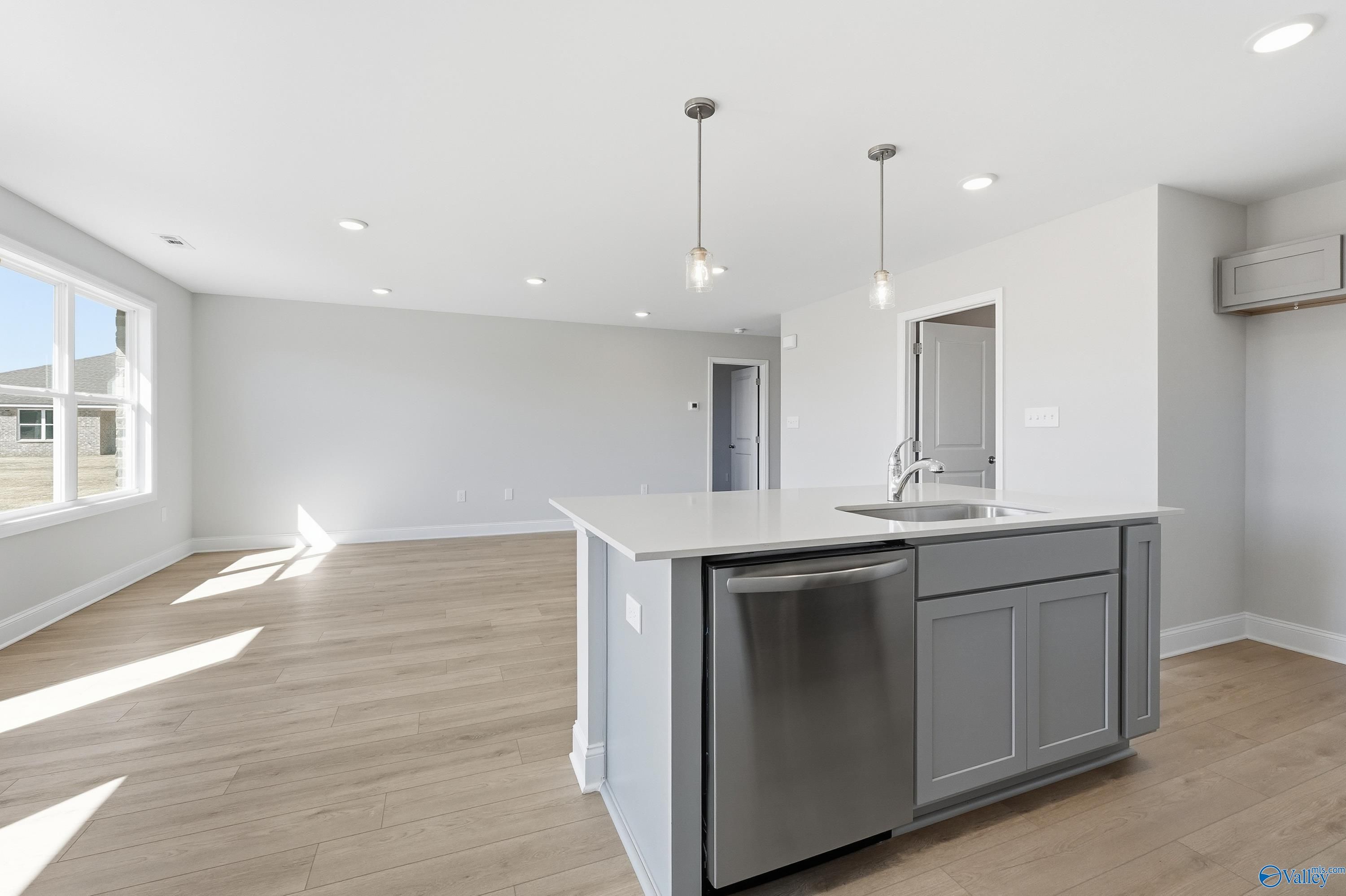 Modern kitchen with white island, stainless dishwasher, gray cabinets, and open living space in The Butler 3-bedroom home, New Market, AL