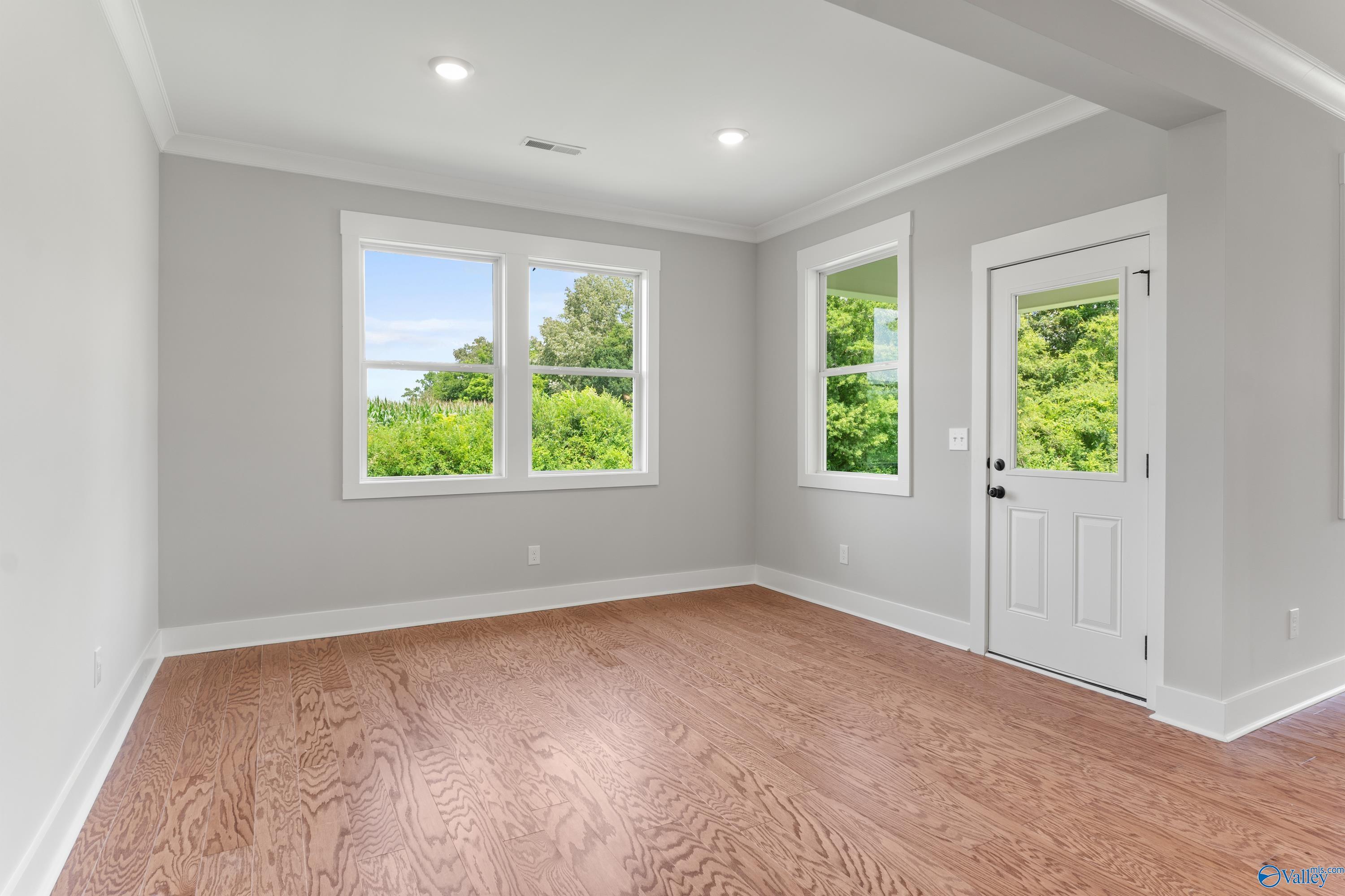 Spacious empty bedroom with oak hardwood floors, gray walls, and large windows overlooking lush greenery in Davidson Homes The Arcadia, Huntsville