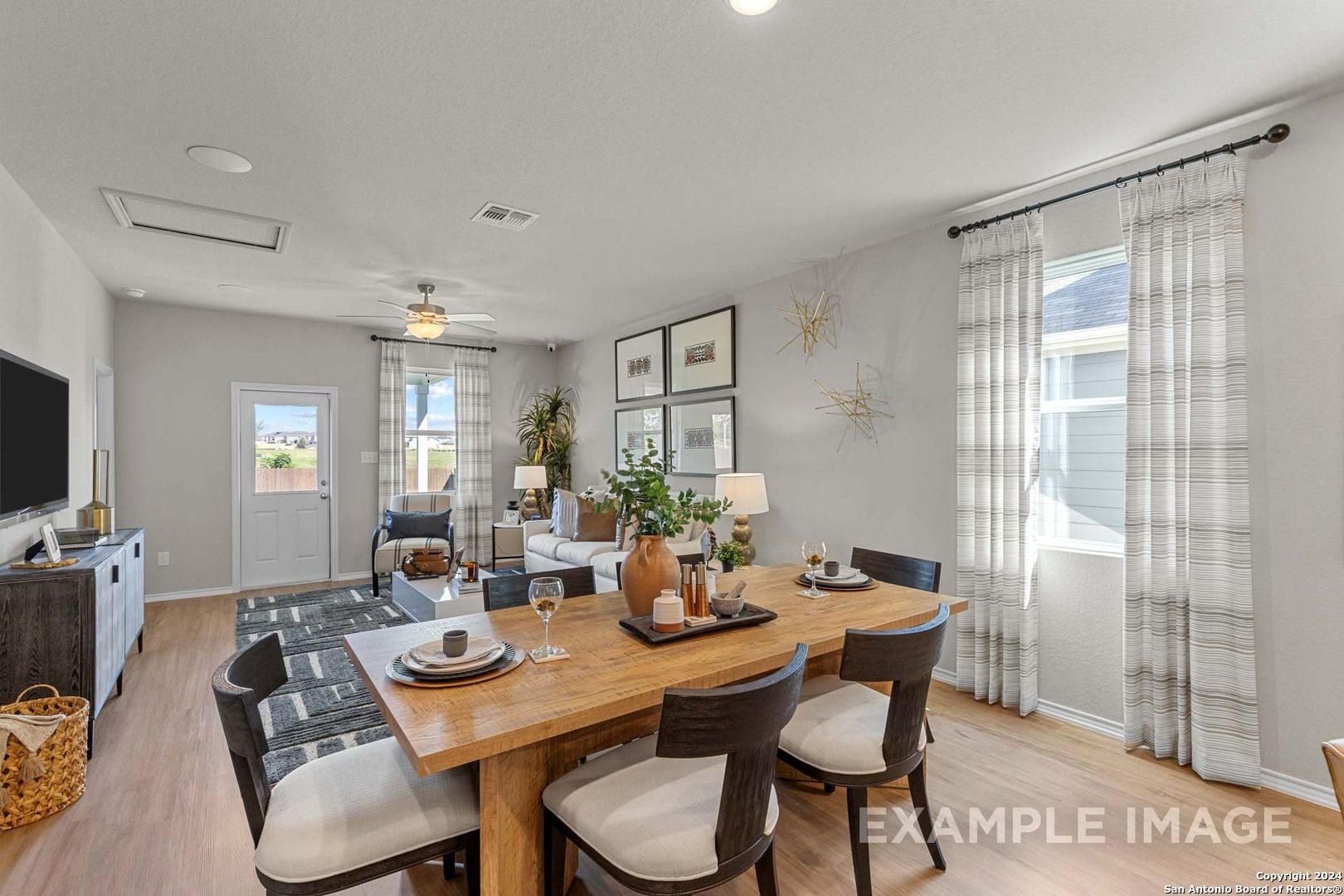Elegant formal dining room with oak table, upholstered chairs, wall-mounted TV, and sheer-curtained windows in The Sabine B, San Antonio home