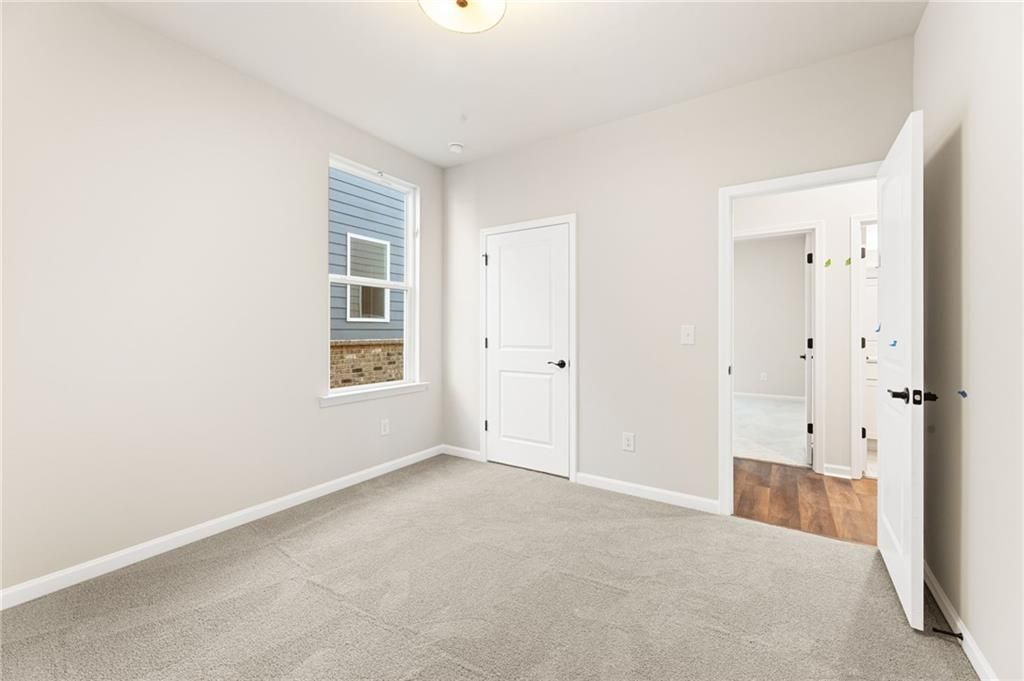 Bright secondary bedroom with en-suite bath, light gray walls, and carpet in Davidson Homes The Glenwood A, Loganville, GA