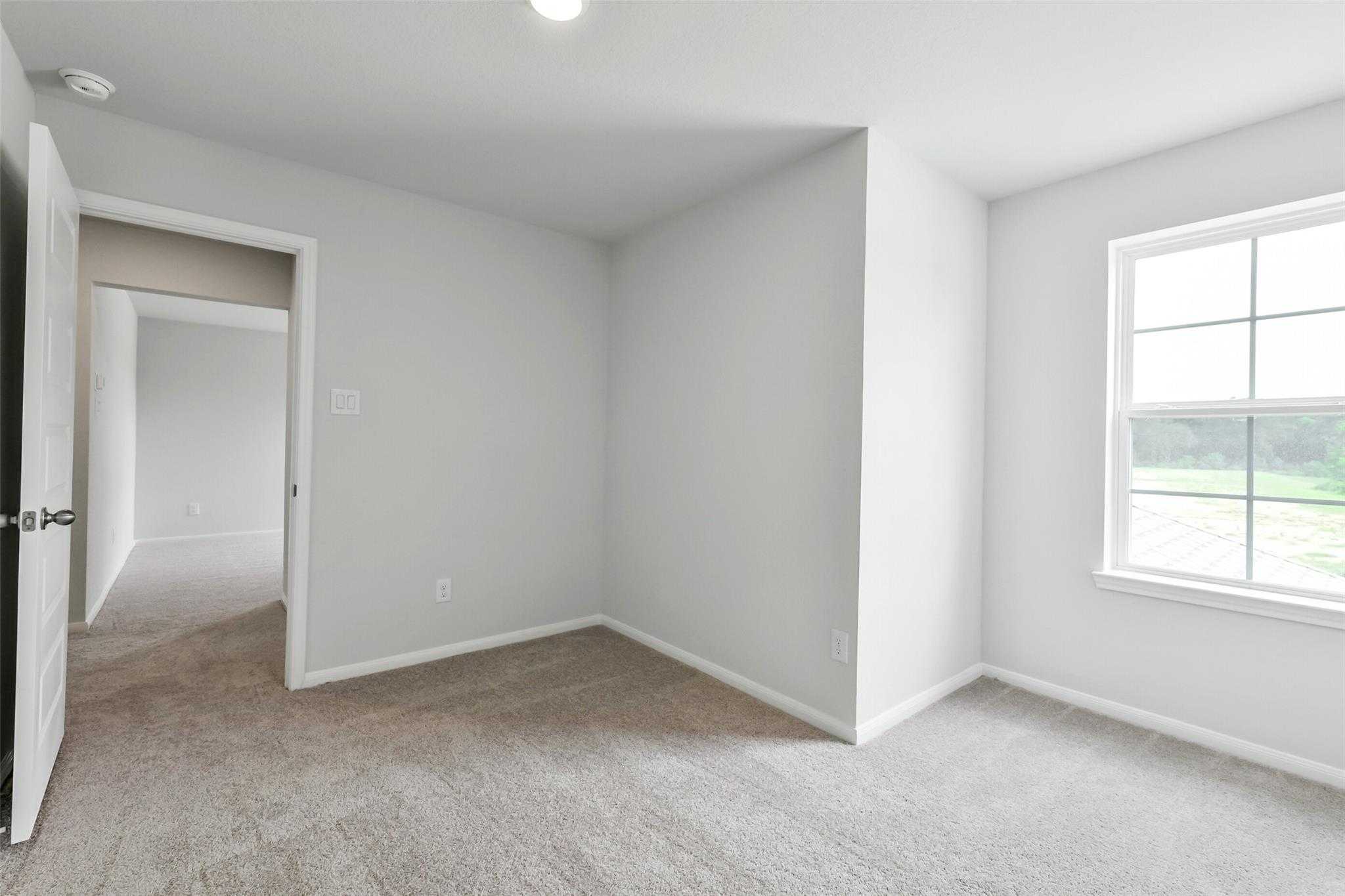 Neutral bedroom with beige carpet, white walls, open doorway, and large window overlooking greenery in Davidson Homes Sabine E, Conroe