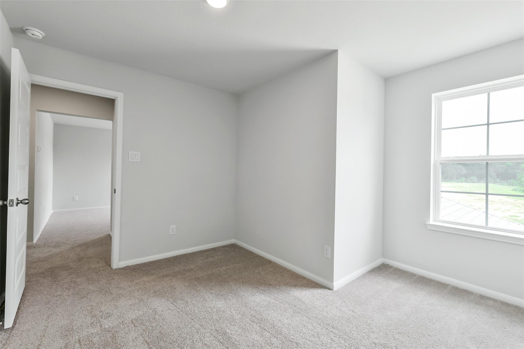 Neutral bedroom with beige carpet, white walls, open doorway, and large window overlooking greenery in Davidson Homes Sabine E, Conroe