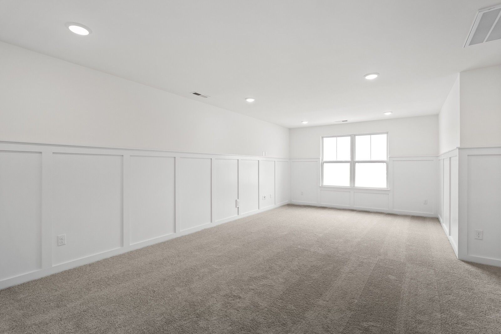 Empty upstairs bedroom with white wainscoting, beige carpet, large window, and recessed lights in Davidson Homes The Ridgeport, Gallatin, TN