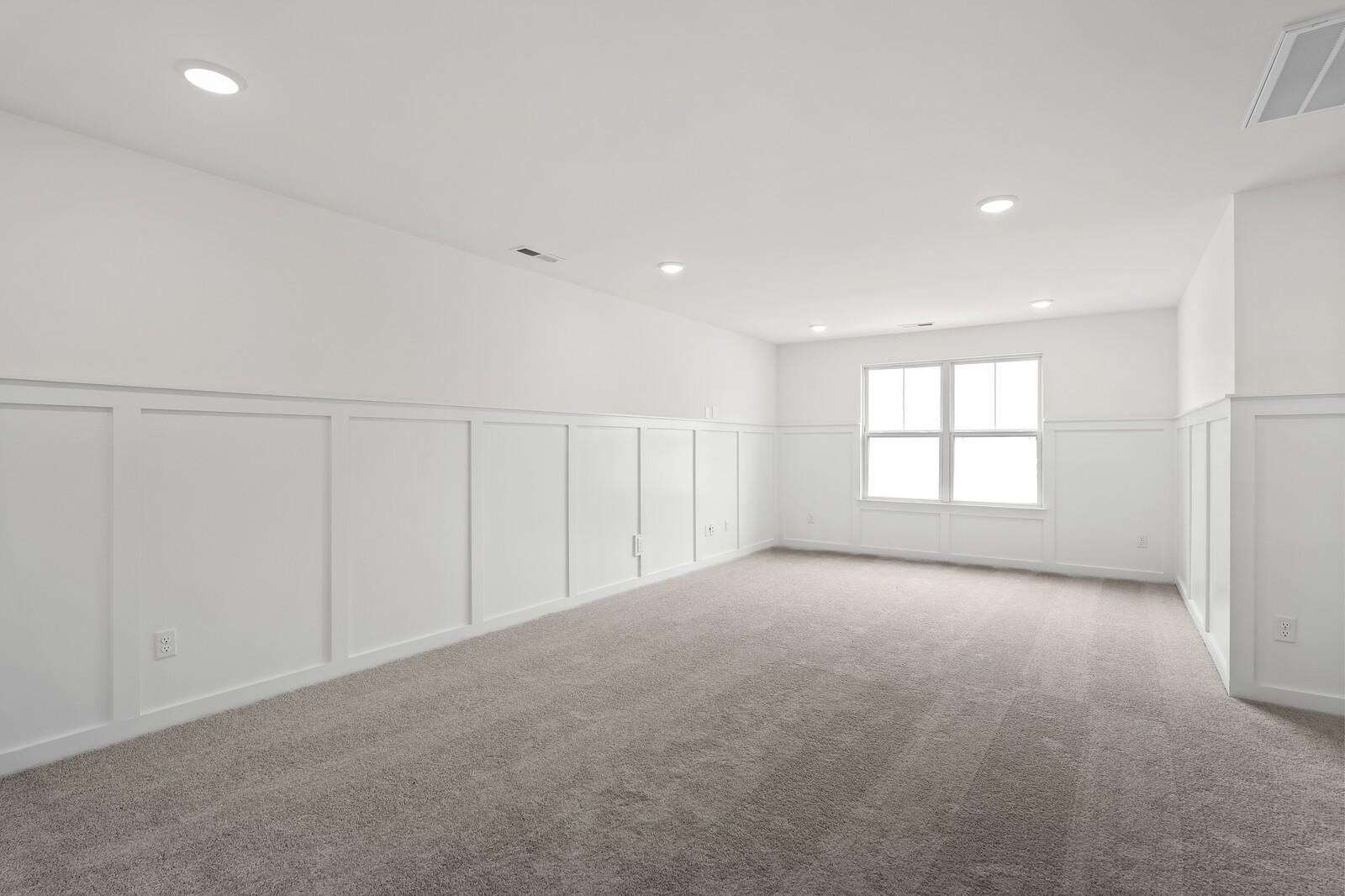 Empty upstairs bedroom with white wainscoting, beige carpet, large window, and recessed lights in Davidson Homes The Ridgeport, Gallatin, TN