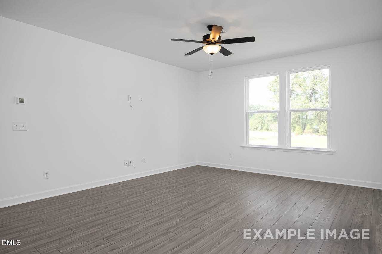 Bright bedroom with ceiling fan, large windows, white walls, and hardwood floors in Davidson Homes The Willow D, Zebulon, NC