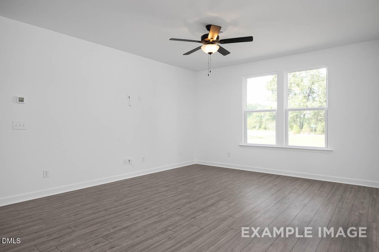 Bright empty bedroom with ceiling fan, large windows to wooded view, and hardwood floors in The Willow D, Zebulon NC