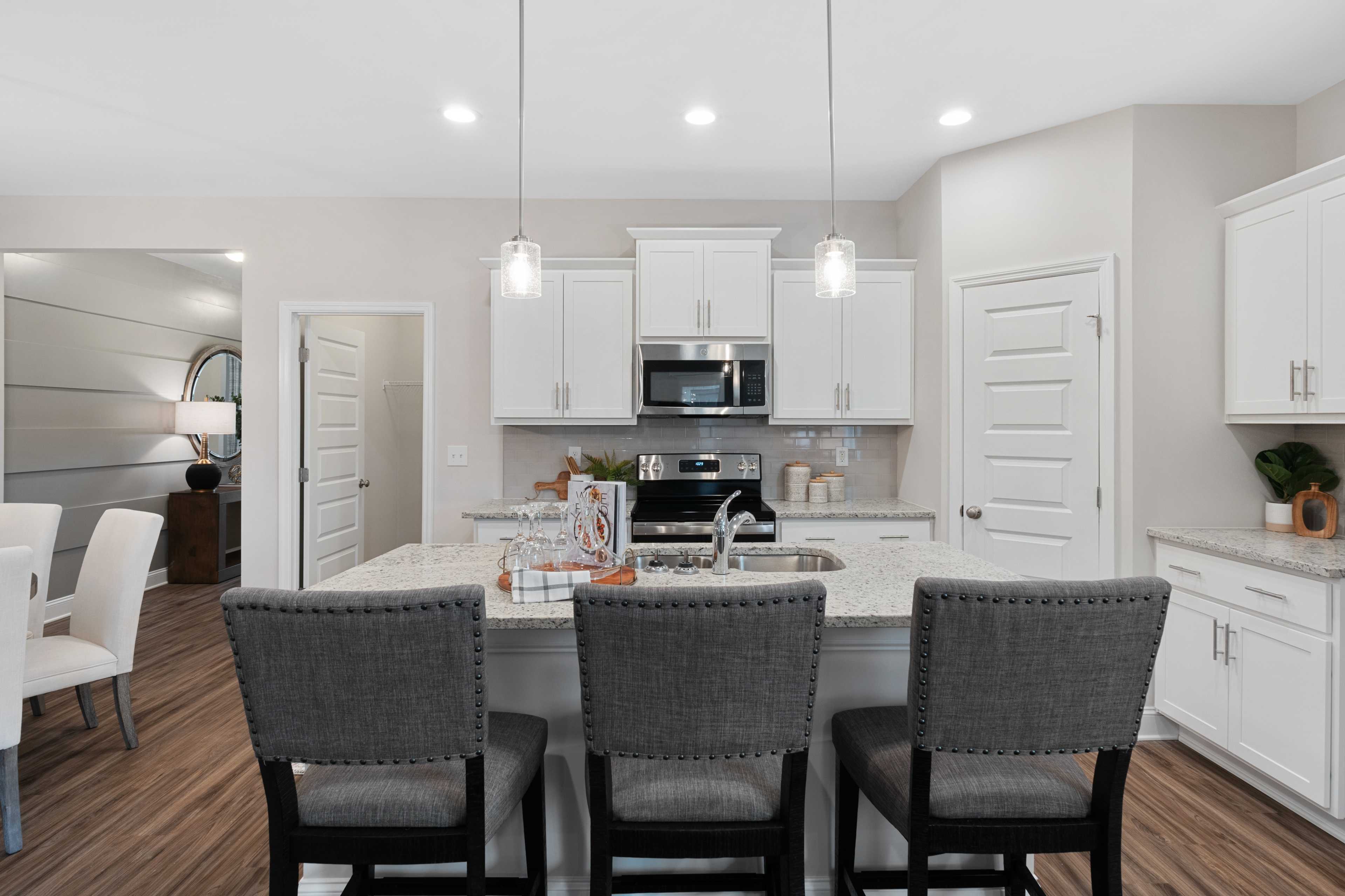Open-concept kitchen at The Retreat at Cain Park in Hartselle AL with white shaker cabinets, large gray island, stainless appliances, hardwood floors