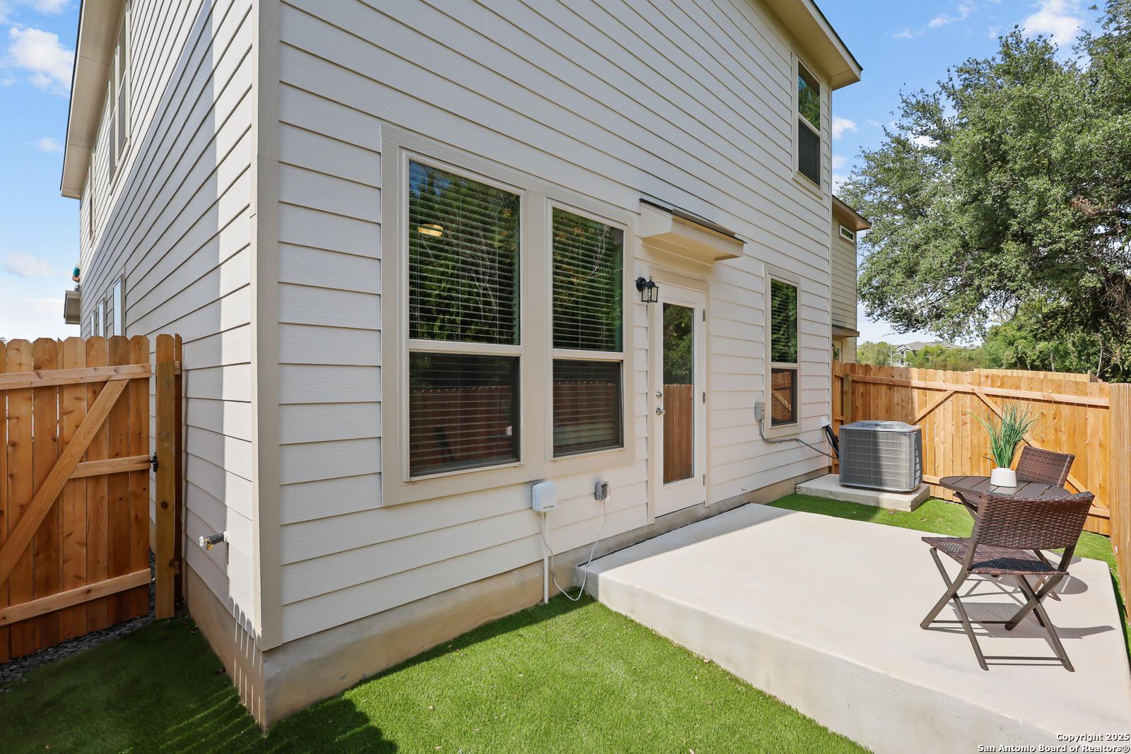 Back exterior of Davidson Homes The Gillian C two-story home with covered patio, wooden fence, artificial turf, and outdoor seating in Cedar Heights, San Antonio, Texas