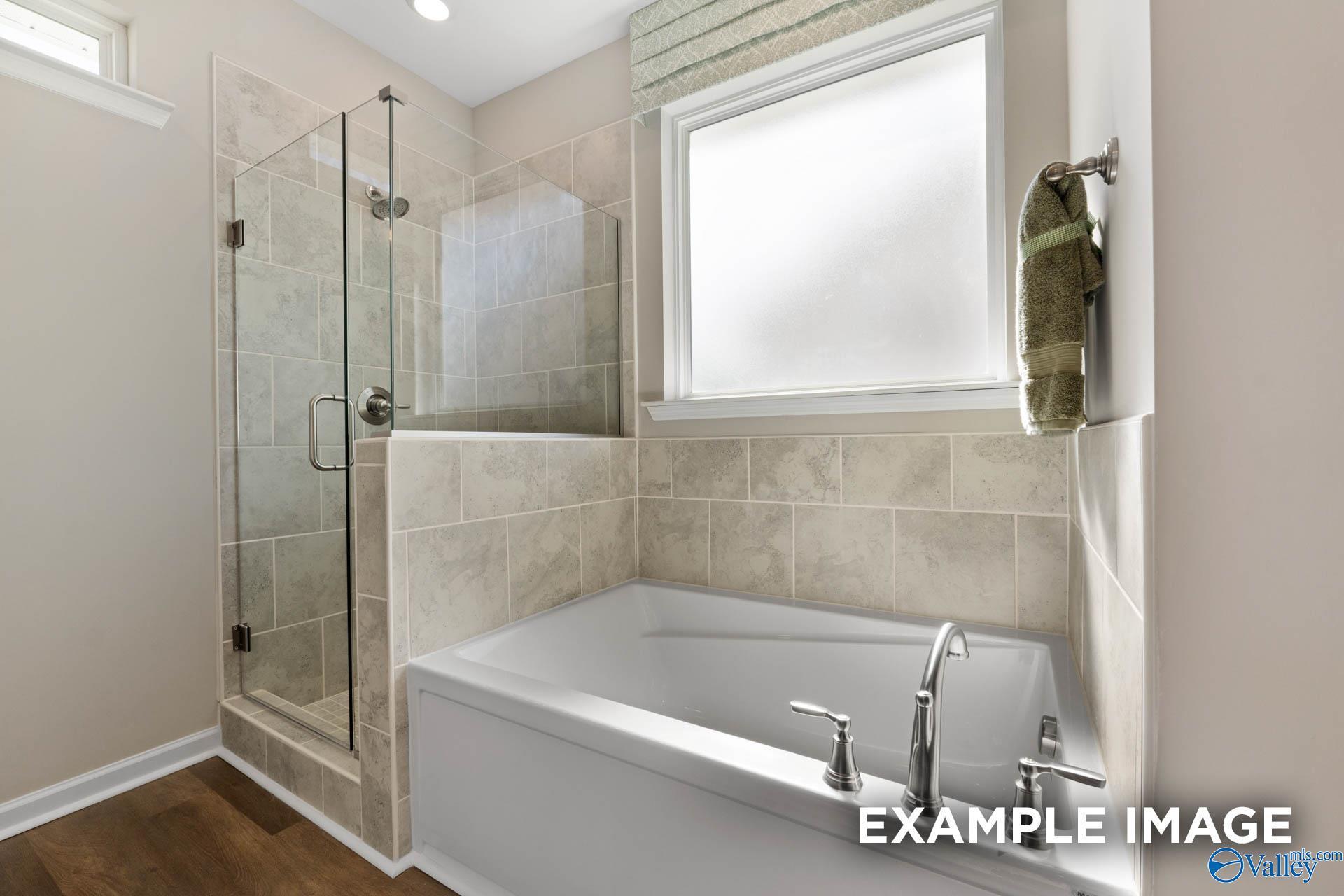 Elegant master bathroom featuring glass shower, soaking tub, tiled walls, and natural light in Davidson Homes The Stella, Madison, Alabama