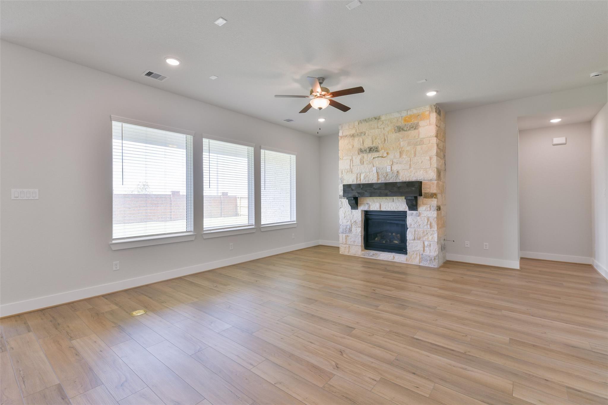 Spacious living room with stone gas fireplace, ceiling fan, hardwood floors and large windows in Davidson Homes The Edward A, Texas City