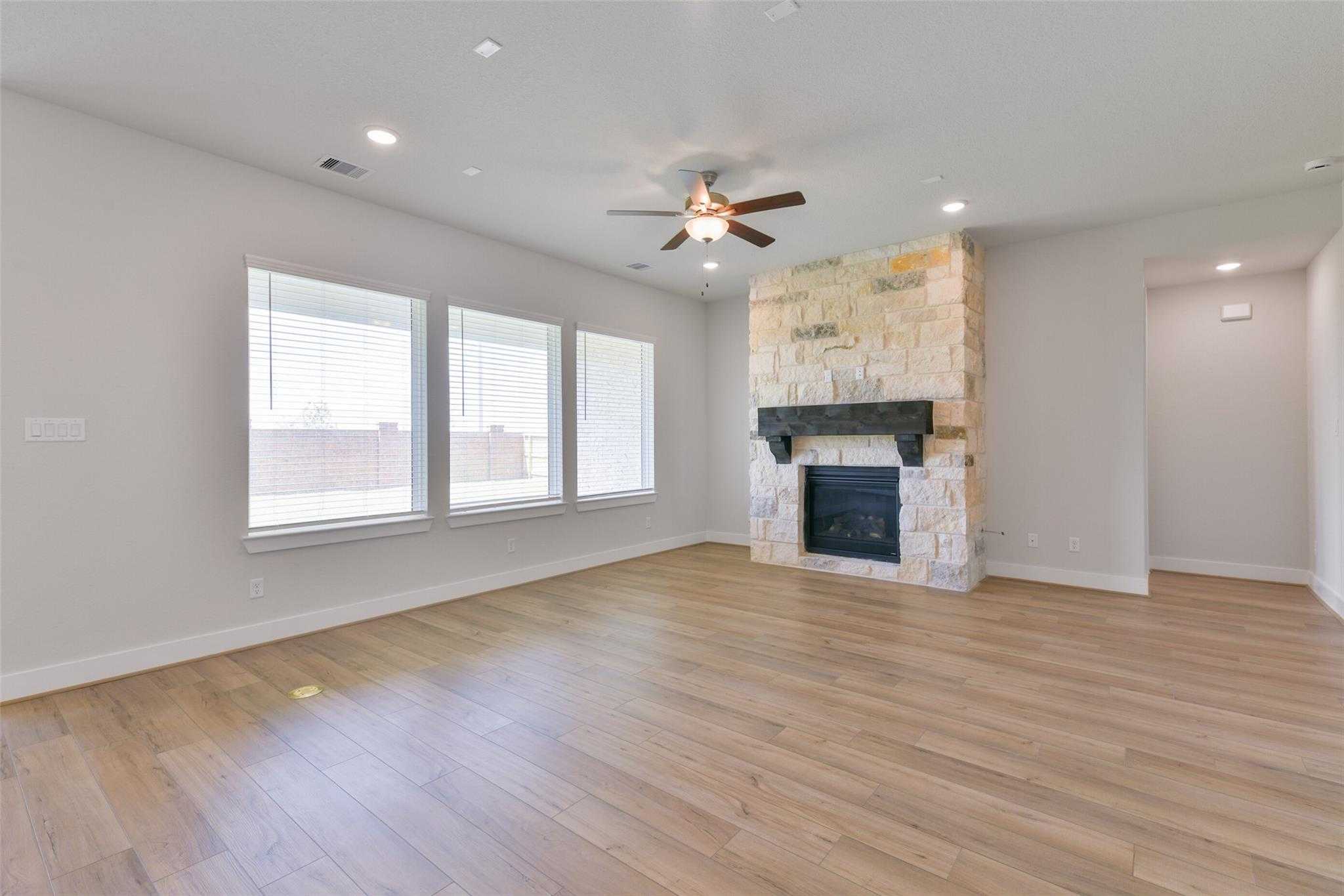 Spacious living room with stone gas fireplace, hardwood floors, ceiling fan, and large windows in Davidson Homes Edward A, Lago Mar, Texas City
