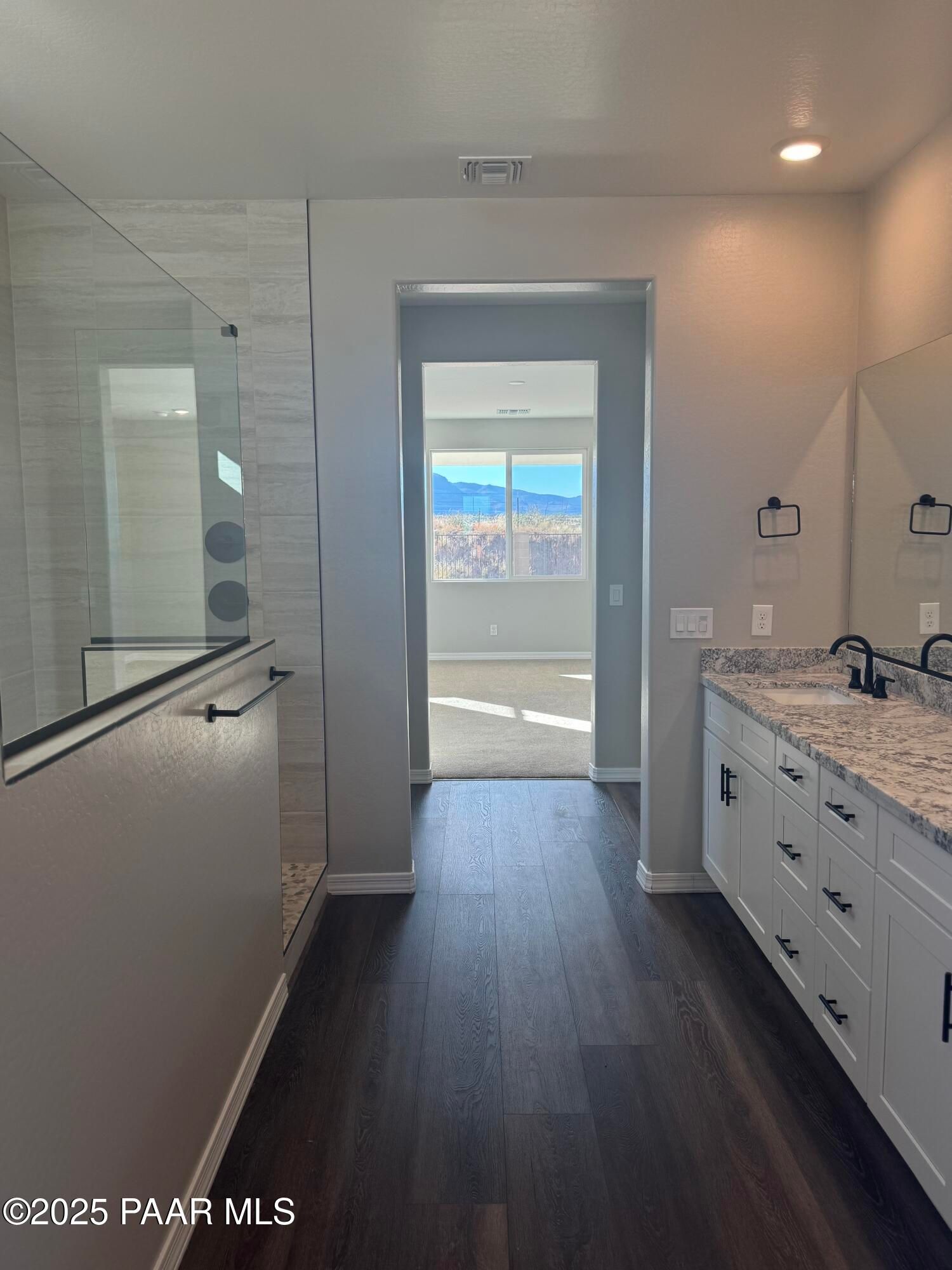 Luxurious master bathroom with frameless glass shower, double quartz vanity, and mountain view through bedroom door in Davidson Homes The Monarch E, Prescott AZ