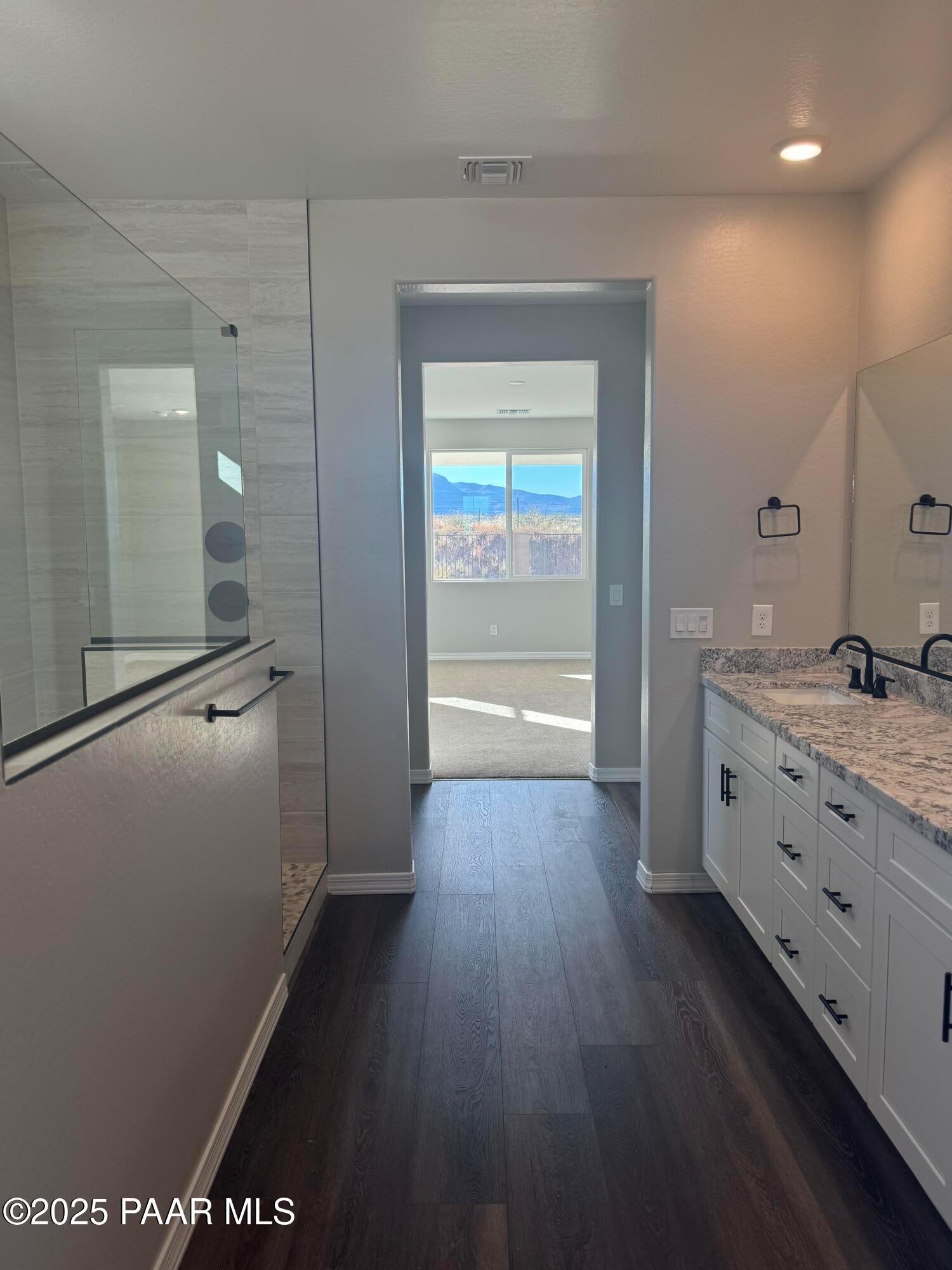 Luxurious master bathroom with frameless glass shower, double quartz vanity, and mountain view through bedroom door in Davidson Homes The Monarch E, Prescott AZ