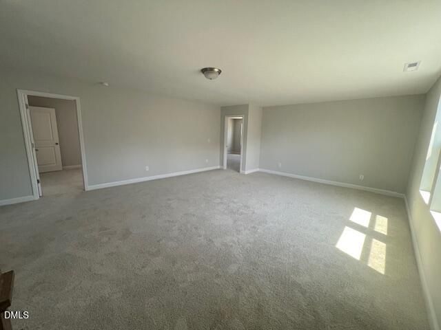 Spacious empty upstairs room with light gray walls, beige carpet, doors, and sunlit windows in Davidson Homes The Adalynn A, Lillington, NC