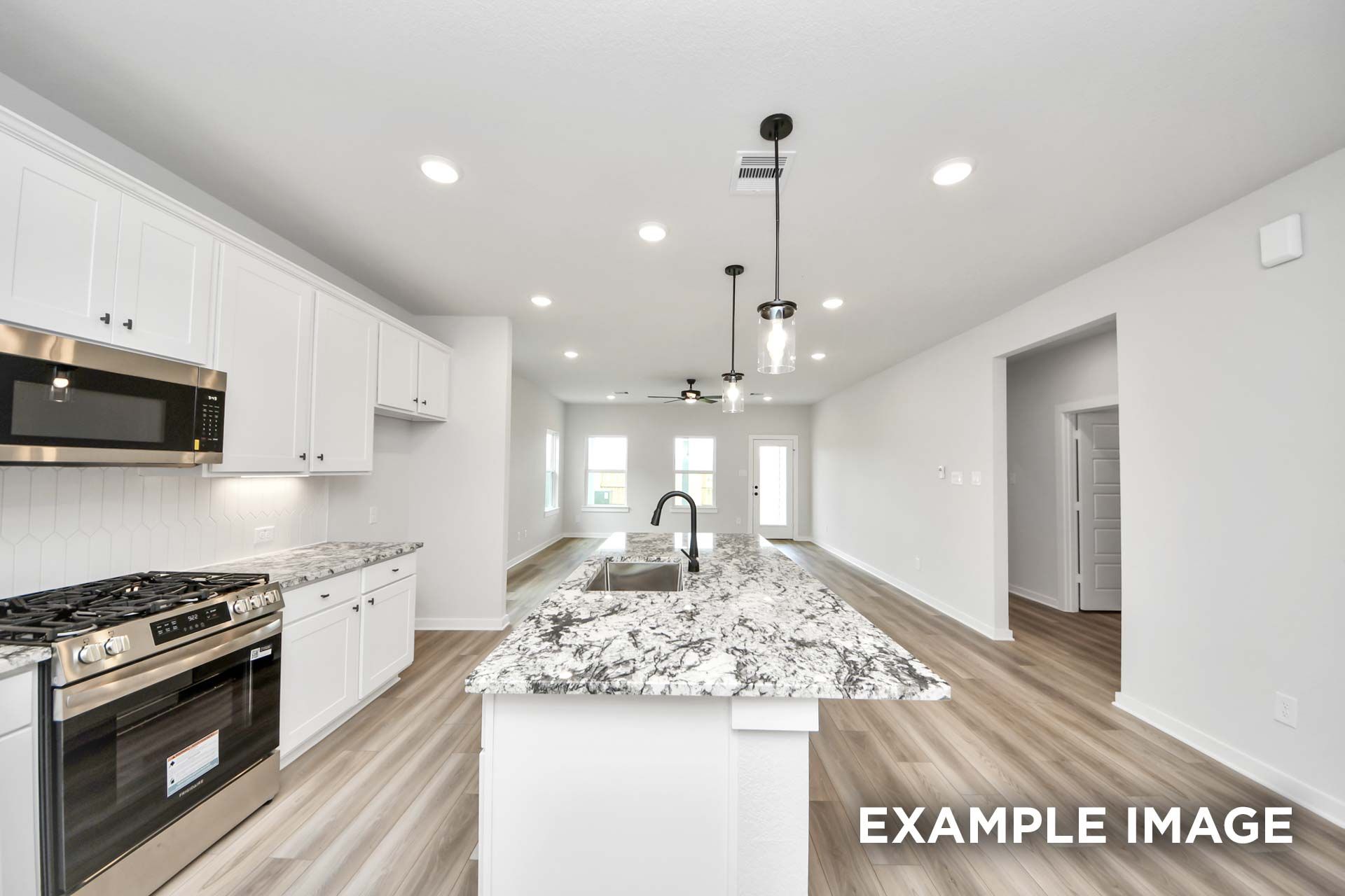 Open-concept kitchen in The Sorrento F featuring a large granite island, white cabinets, and modern stainless appliances.