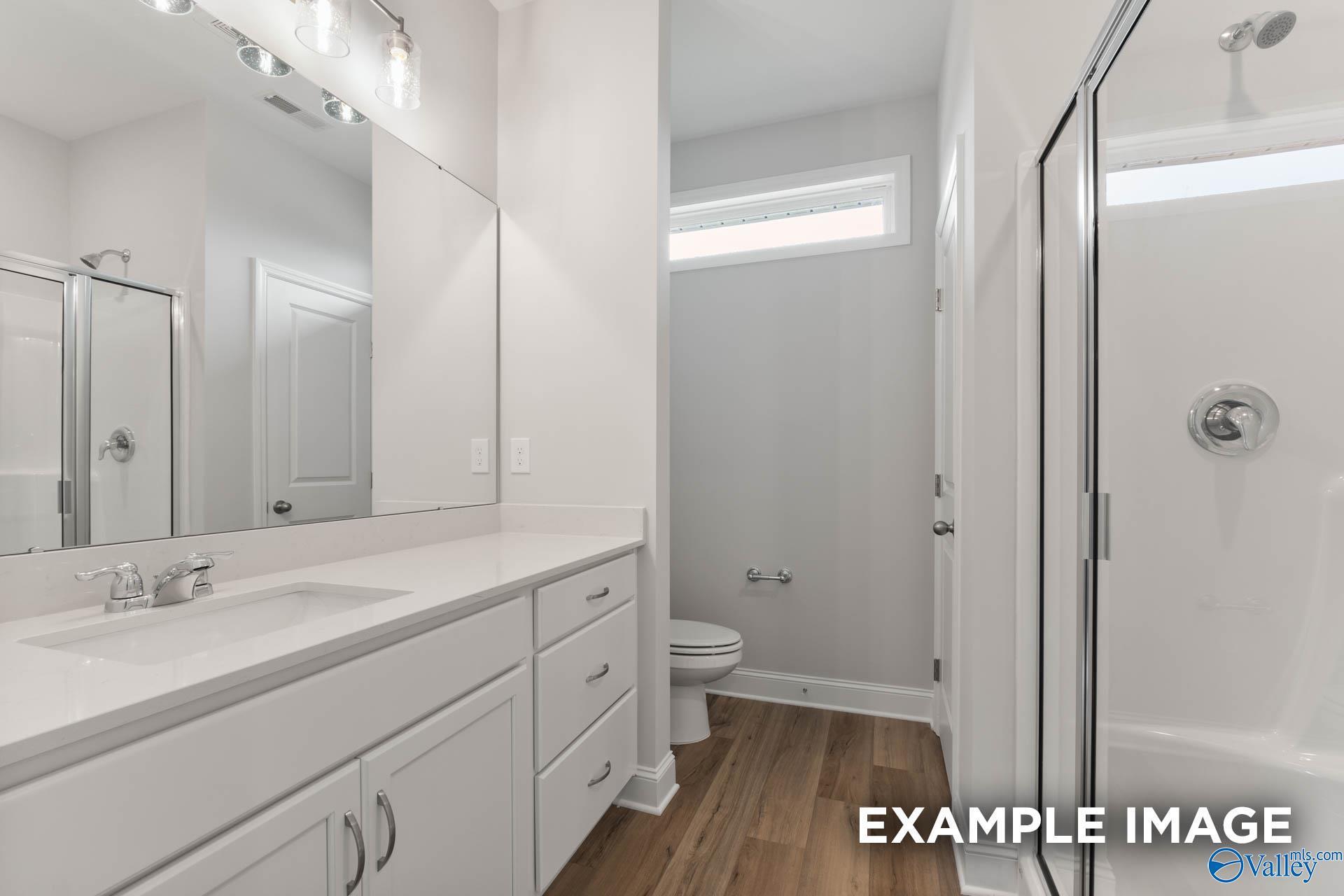 Modern bathroom with white vanity, large mirror, and glass-enclosed shower in The Butler floor plan, Heritage Lakes.