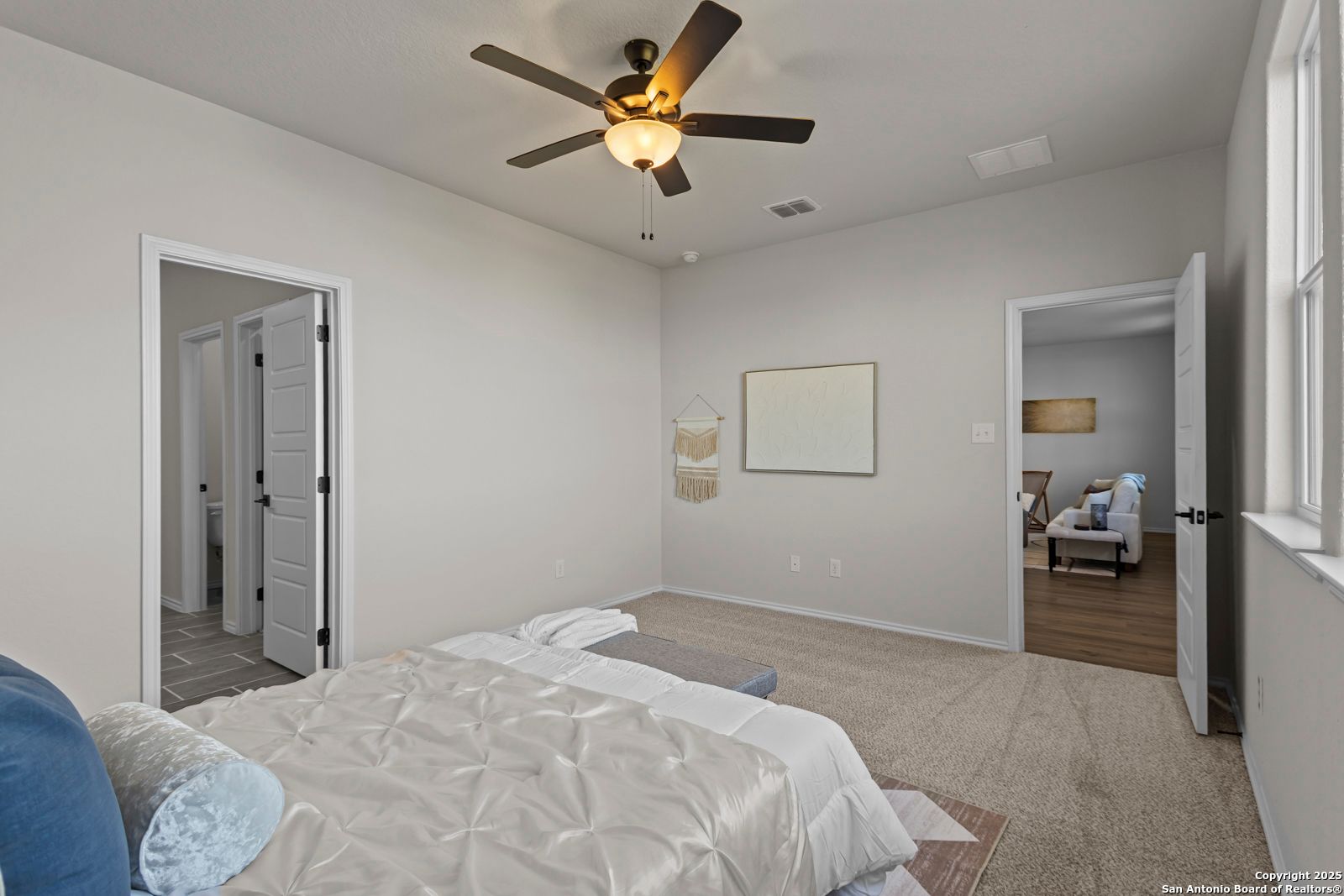 Cozy secondary bedroom with ceiling fan, tufted white bedding, blue pillows, and en-suite bath door in Davidson Homes The Douglas C, Seguin, Texas