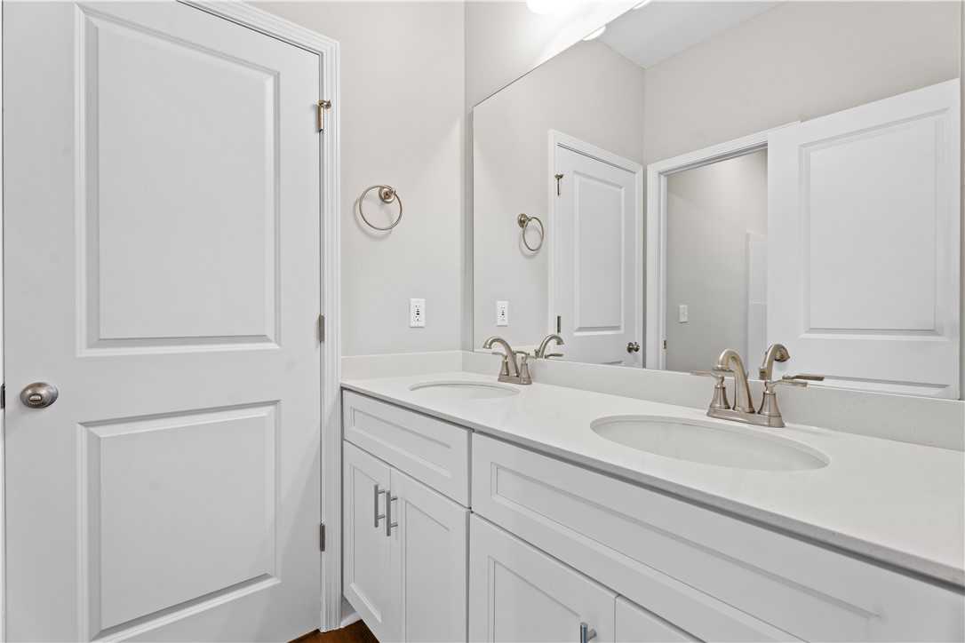 Modern double-vanity bathroom with white cabinets, chrome faucets, and mirrors in Evermore Homes The Orion, Cusseta, Alabama