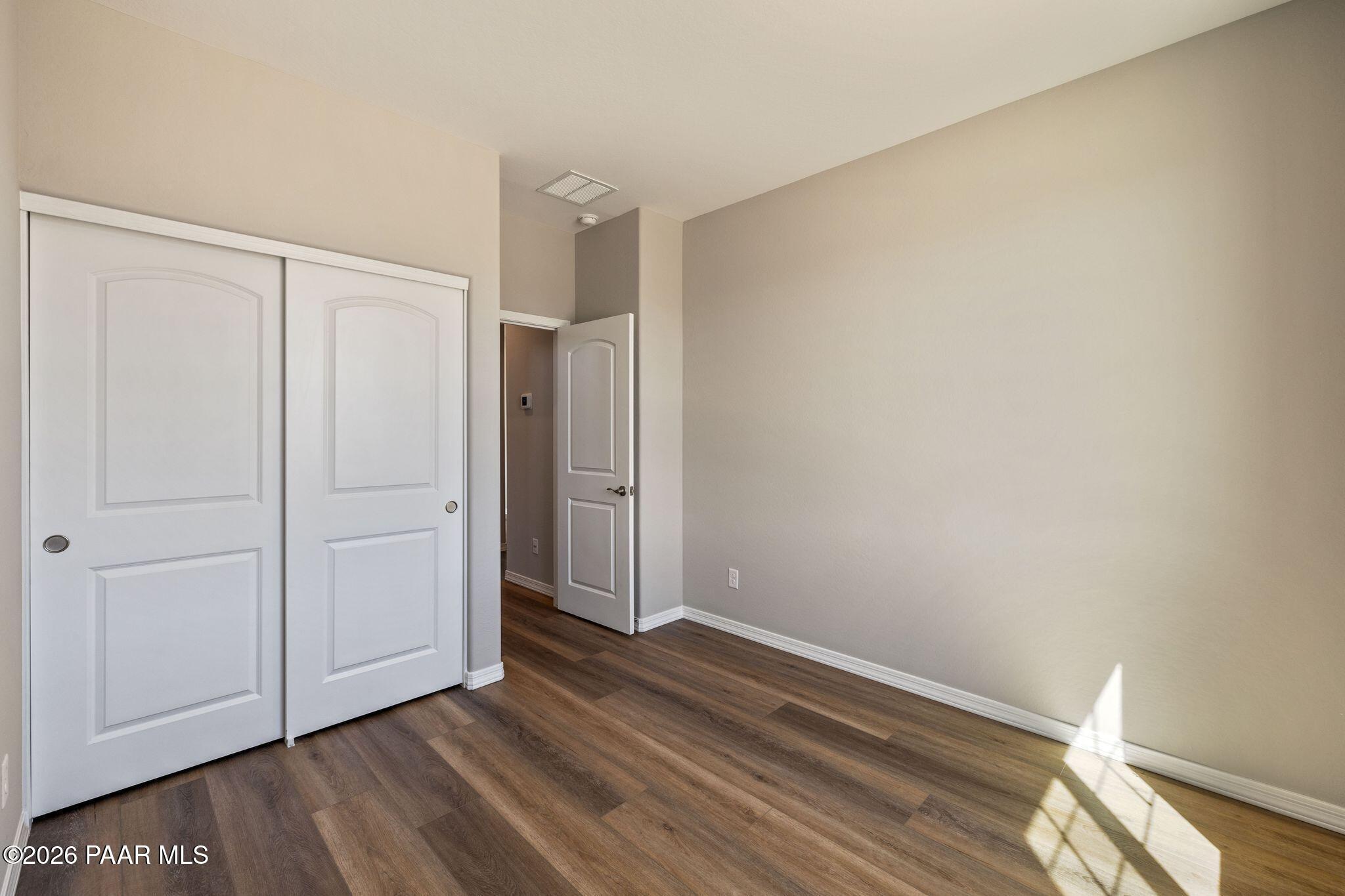 Spacious secondary bedroom with white sliding closet doors, beige walls, and luxury vinyl plank flooring in Davidson Homes The Frontier A, Prescott Valley