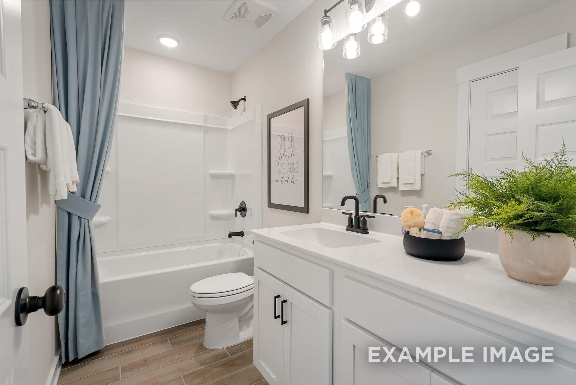 Bright bathroom with white vanity, soaking tub, blue curtains, and wood floors in Davidson Homes Ridgeport, Gallatin, Tennessee