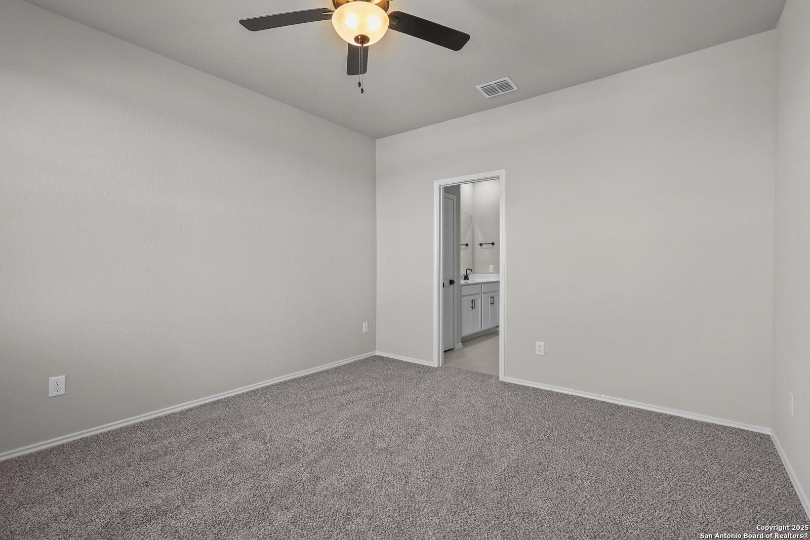 Spacious empty bedroom with ceiling fan, neutral walls, carpet, and attached bath in Davidson Homes The Brazos C, San Antonio