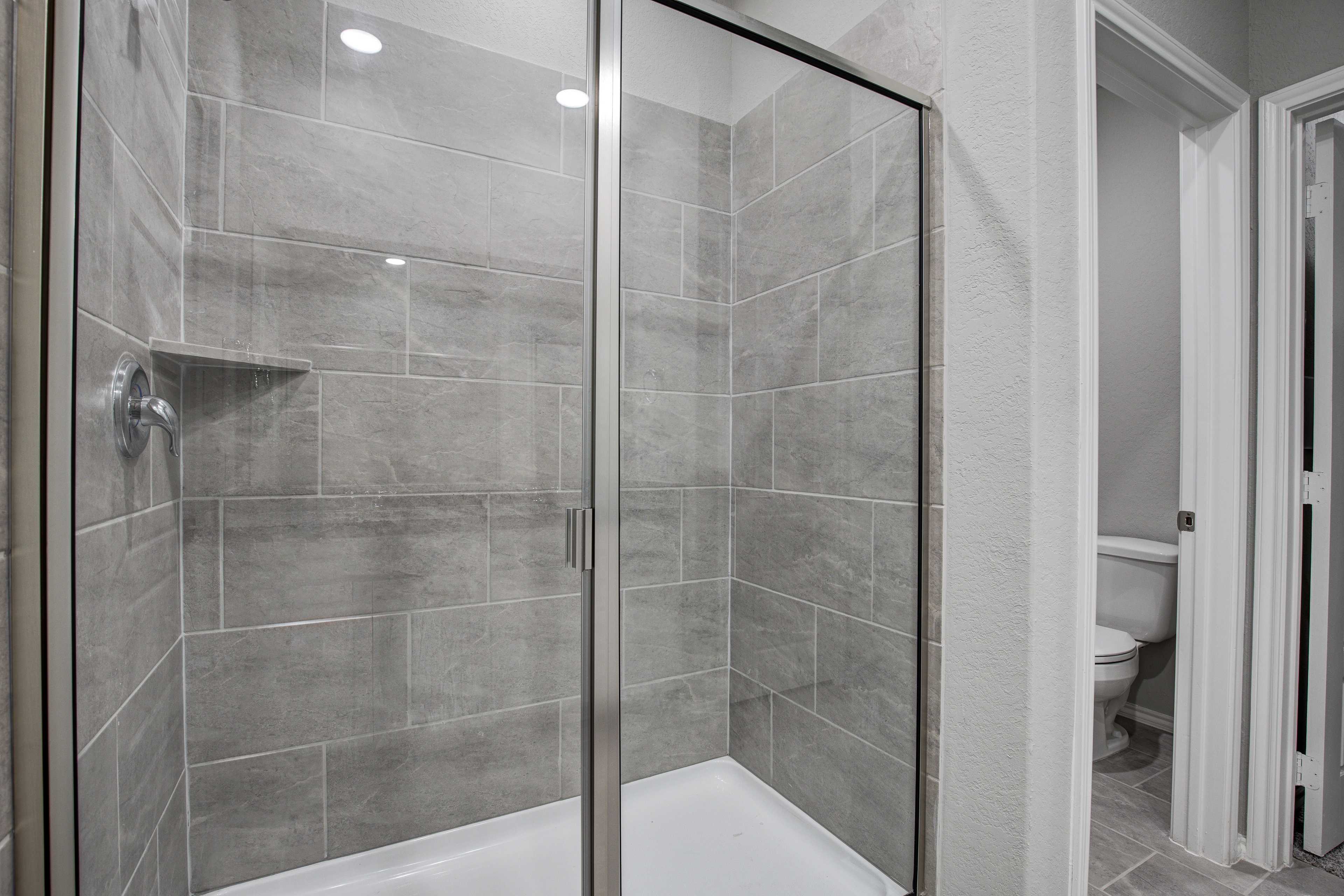 Master bathroom in The Asheville by Davidson Homes featuring frameless glass shower with gray tile walls and open toilet area