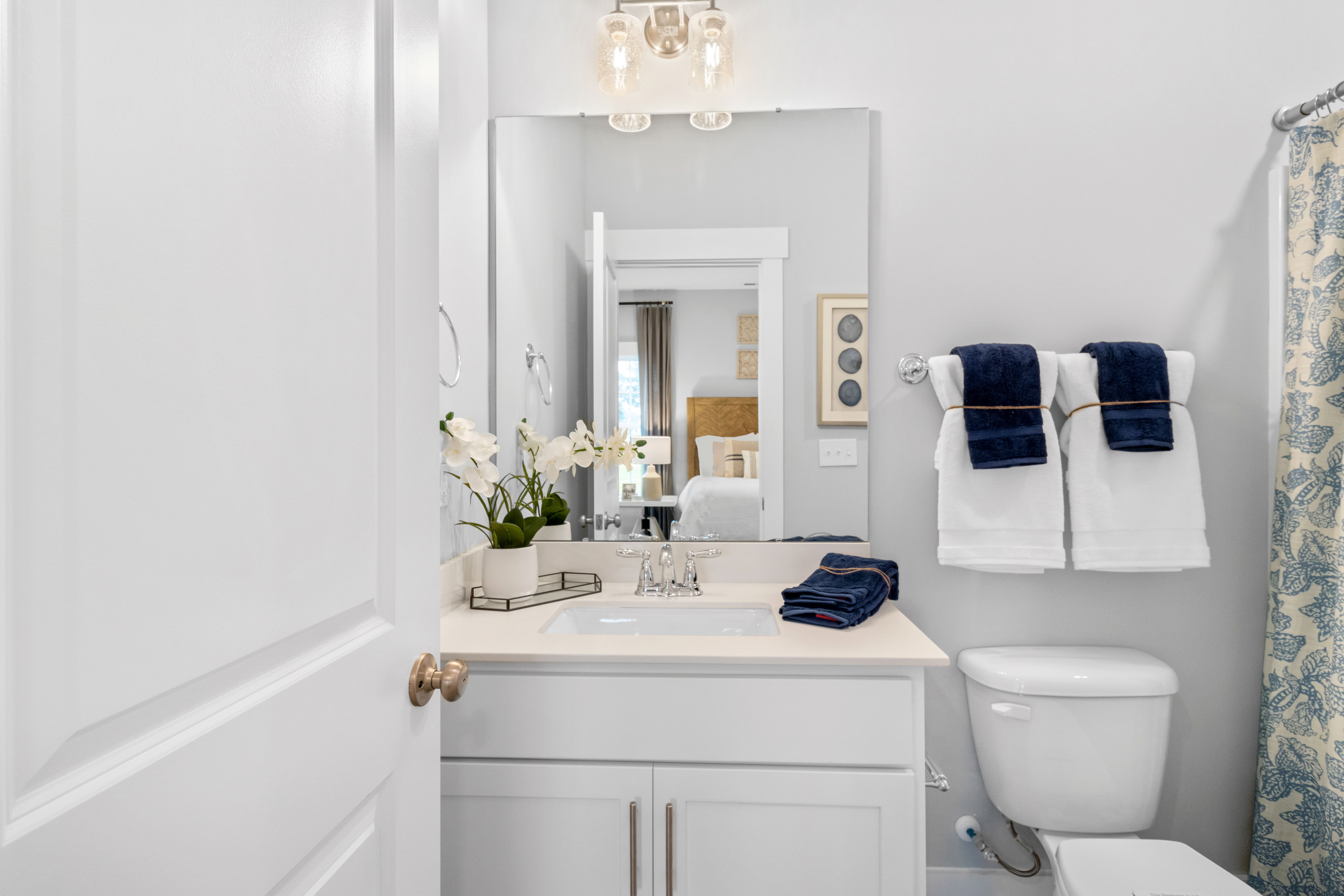 Spacious modern bathroom at Noble Ridge in Cullman Alabama with white vanity, navy towels, blue shower curtain, and orchids