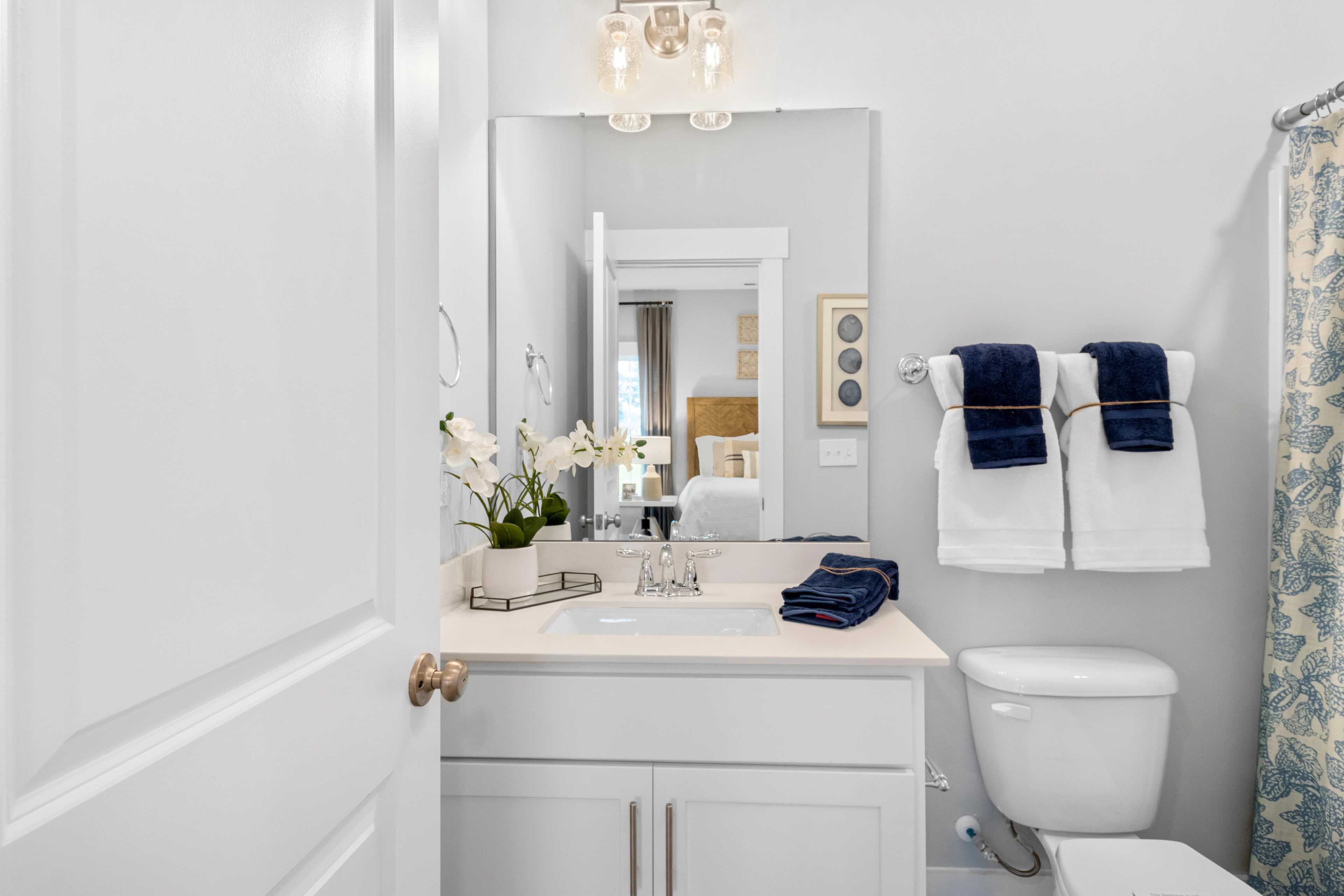 Spacious modern bathroom at Noble Ridge in Cullman Alabama with white vanity, navy towels, blue shower curtain, and orchids
