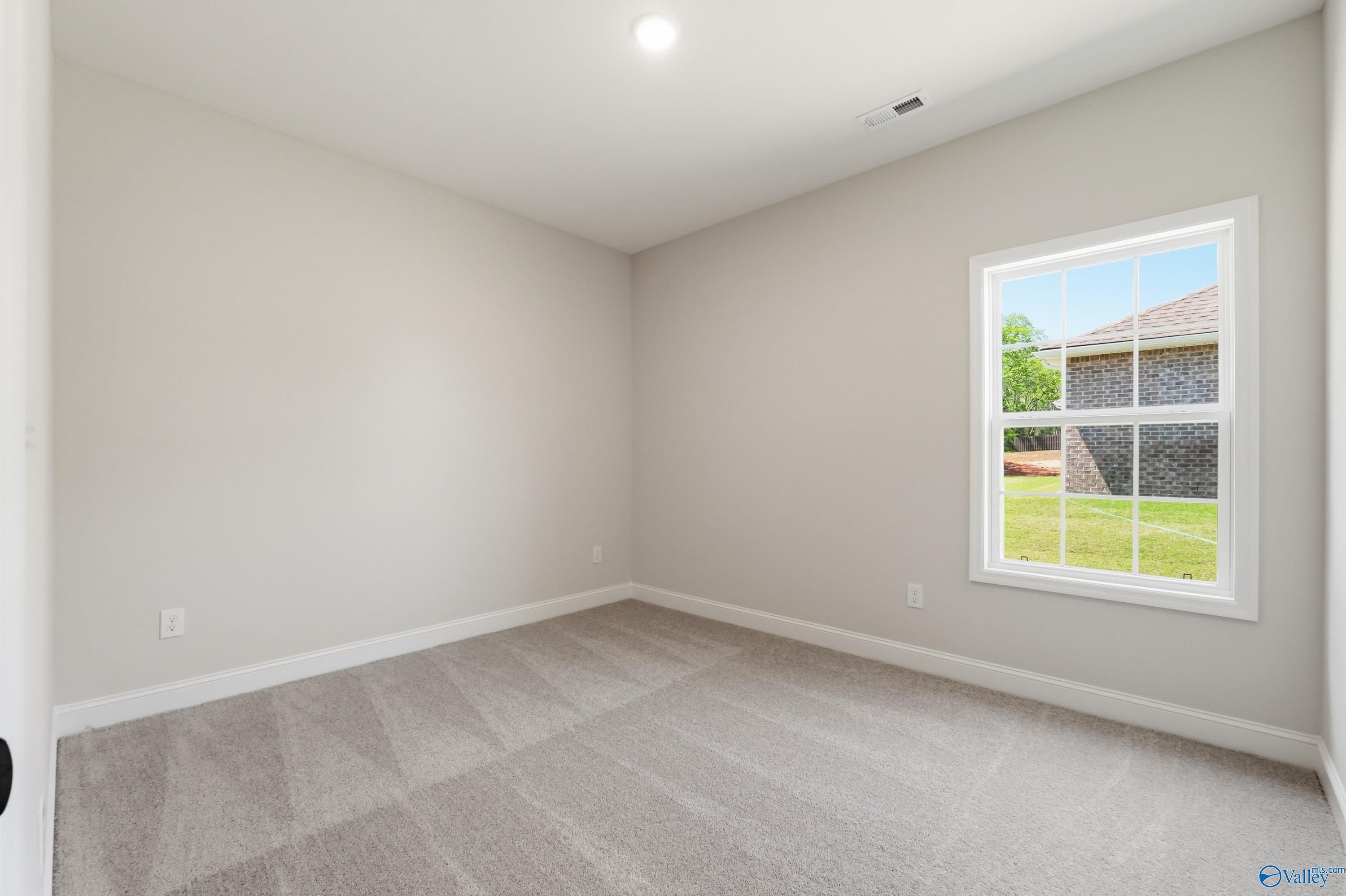 Bright secondary bedroom with beige walls, neutral carpet, and large window overlooking green backyard in The Rockford B, Athens, AL