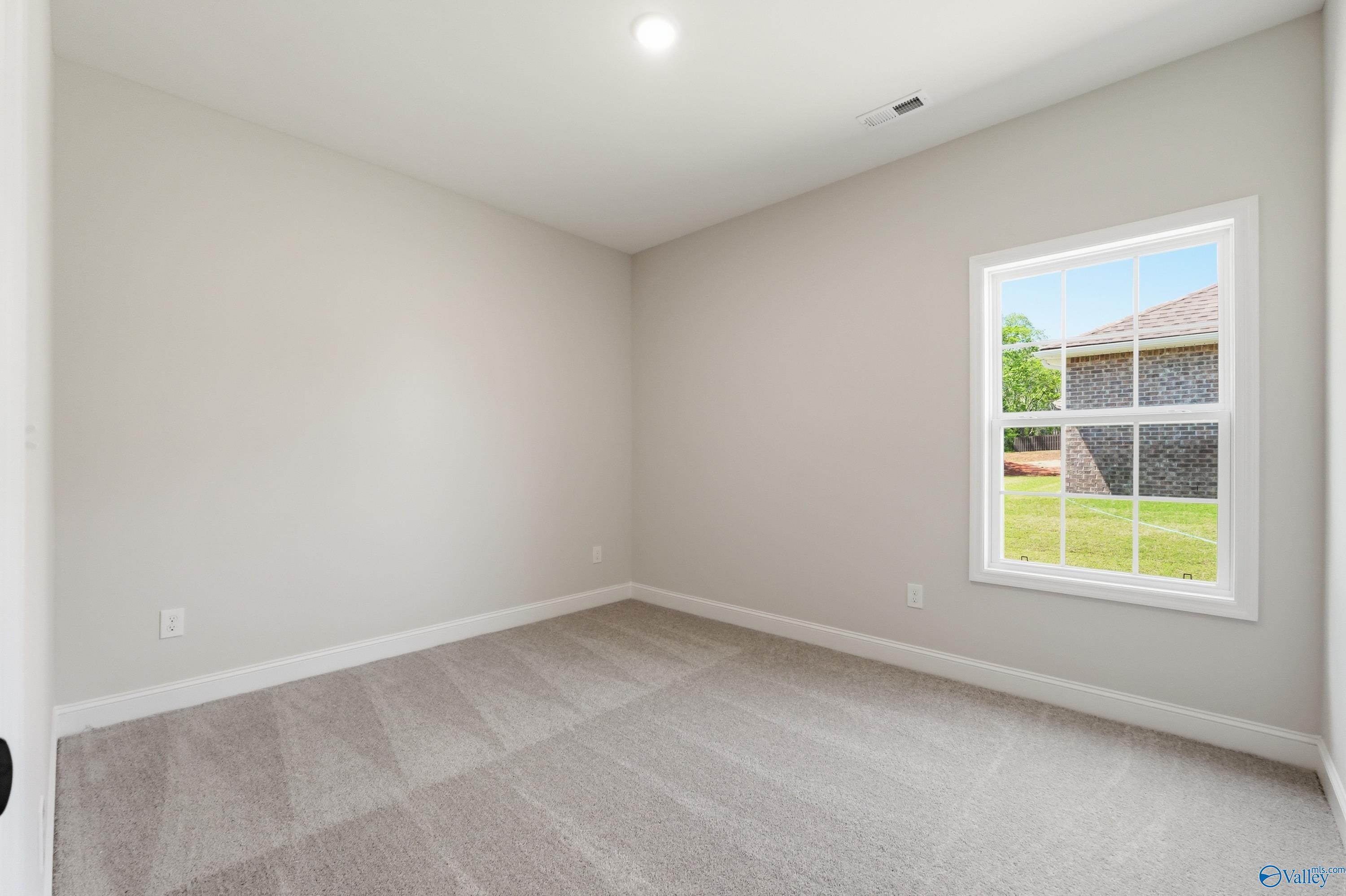 Bright secondary bedroom with beige walls, neutral carpet, and large window overlooking green backyard in The Rockford B, Athens, AL