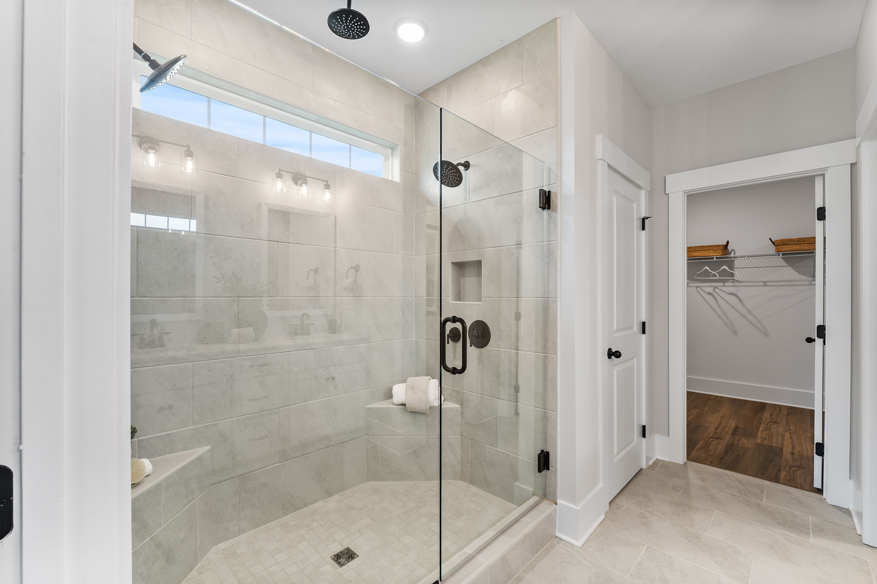 Luxurious primary bathroom at River Road Estates in Decatur AL with frameless glass shower, subway tile, bench, and walk-in closet