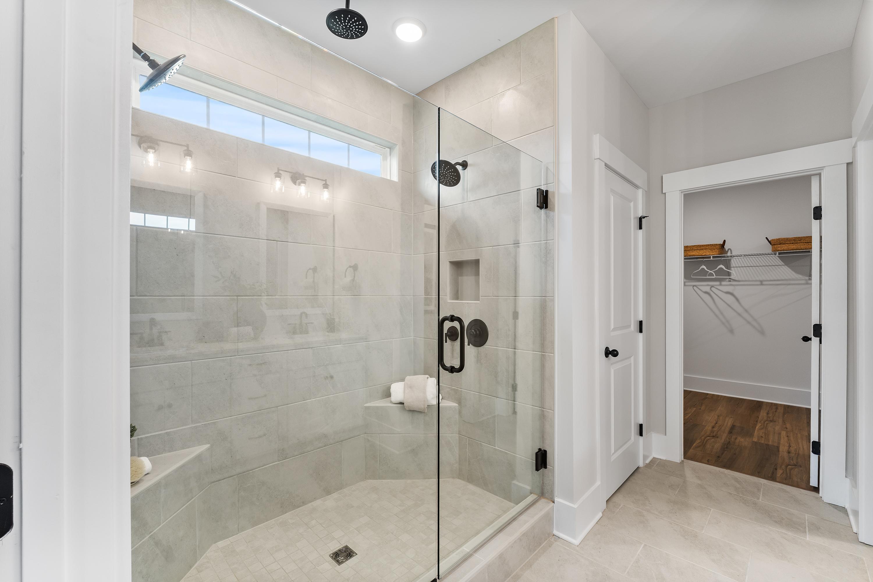 Luxurious primary bathroom at River Road Estates in Decatur AL with frameless glass shower, subway tile, bench, and walk-in closet