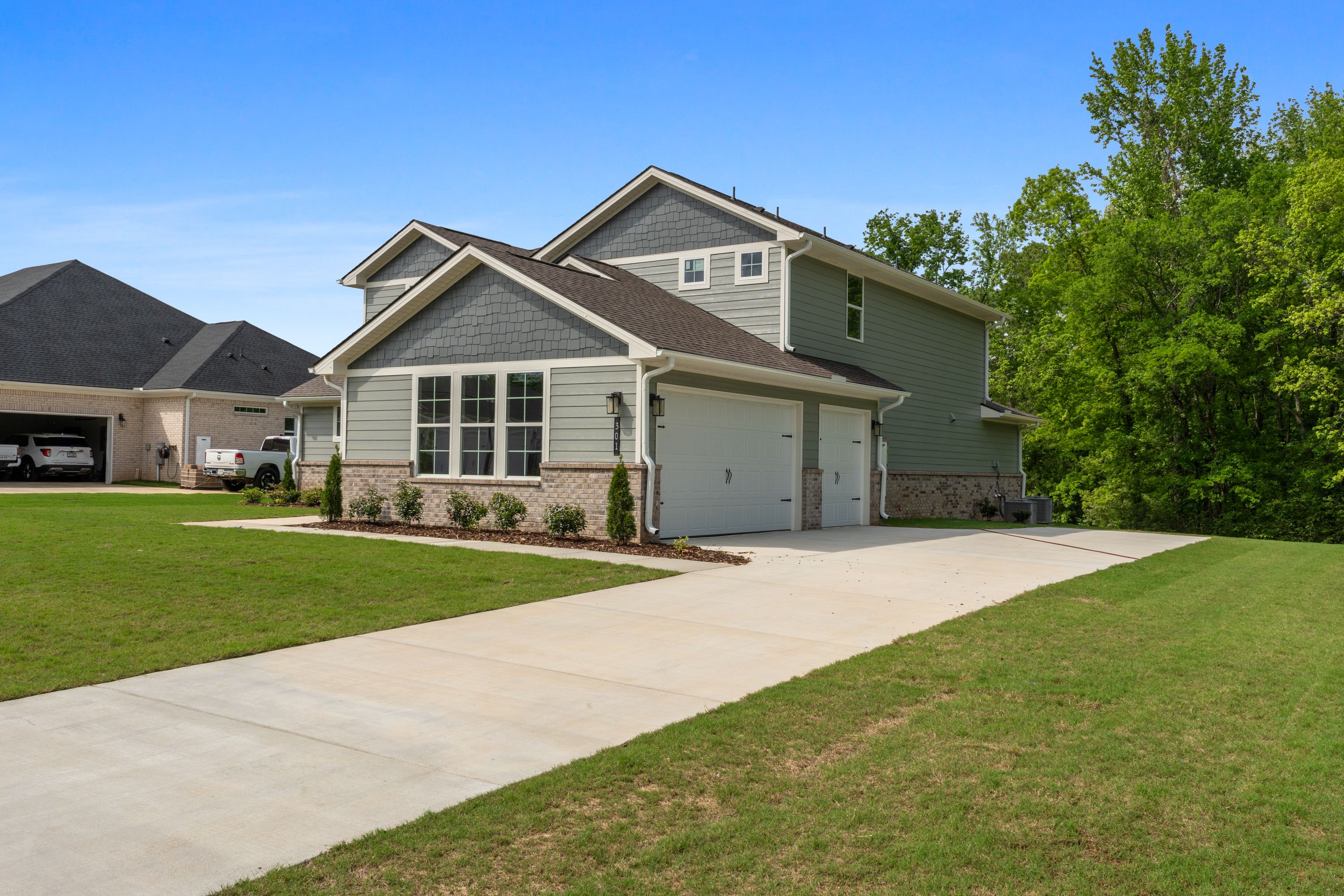 Two-story Avalon D home exterior with gray siding, three-car garage, brick accents, and lush green lawn