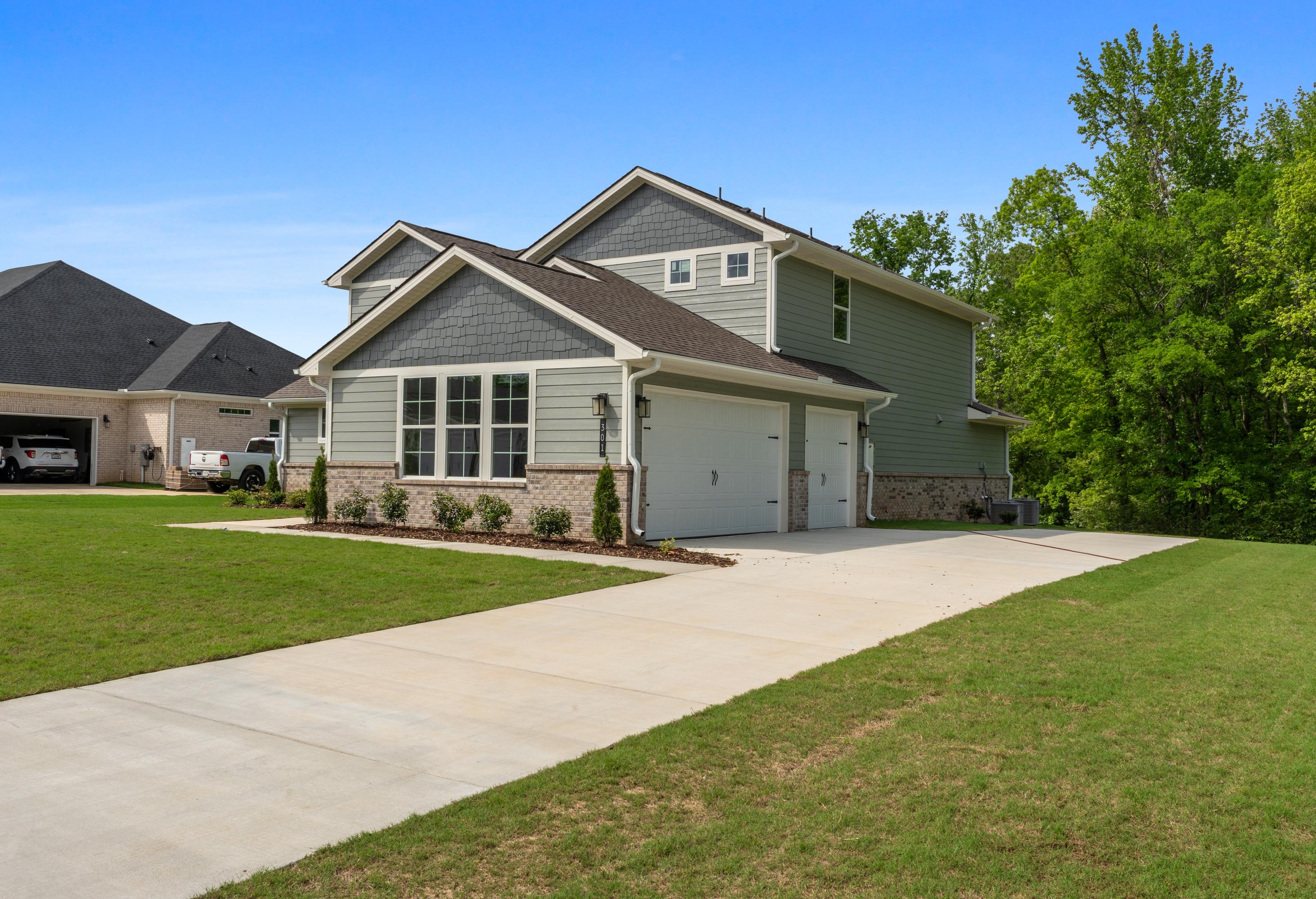 Two-story Avalon D home exterior with gray siding, three-car garage, brick accents, and lush green lawn