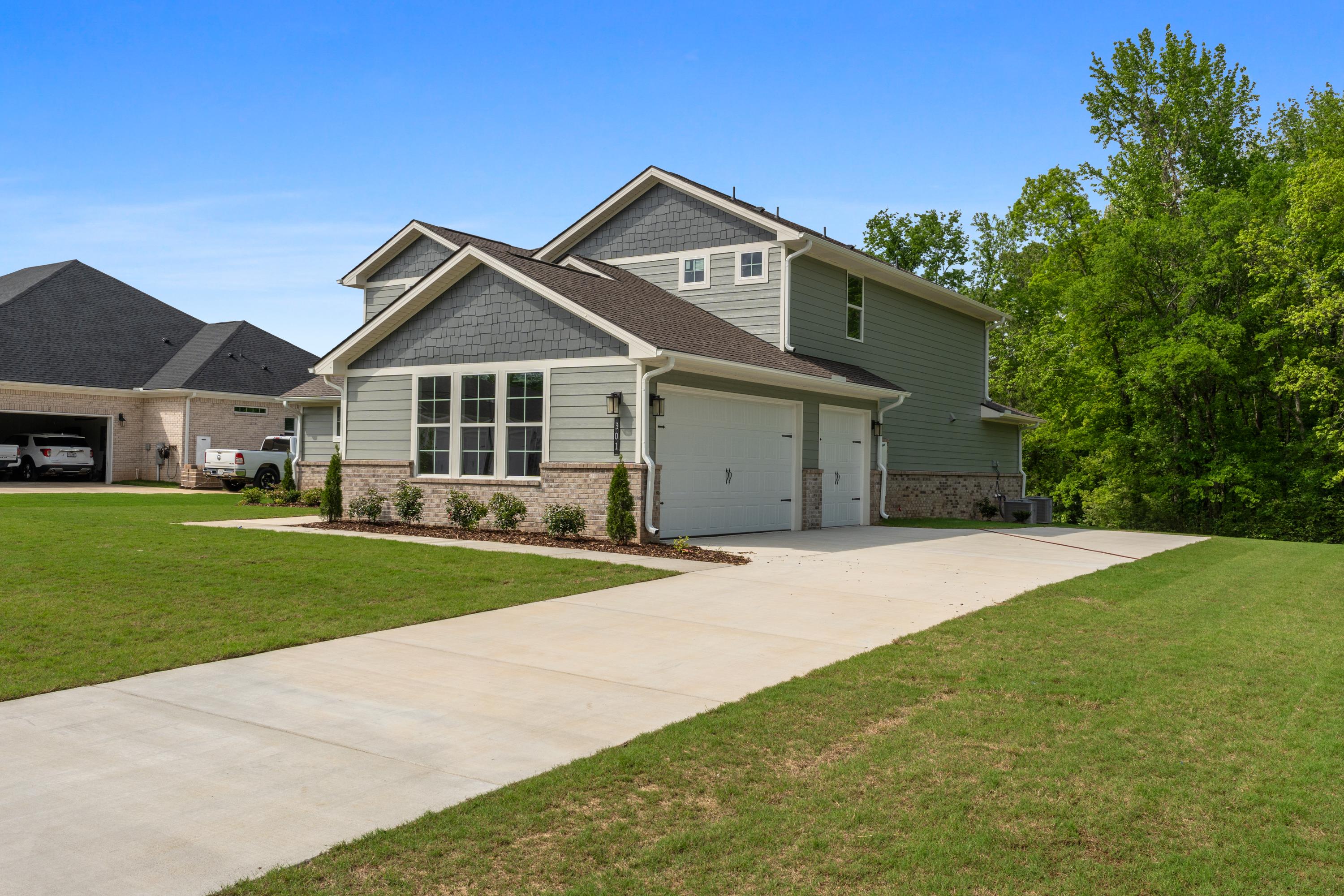 Two-story Avalon D home exterior with gray siding, three-car garage, brick accents, and lush green lawn