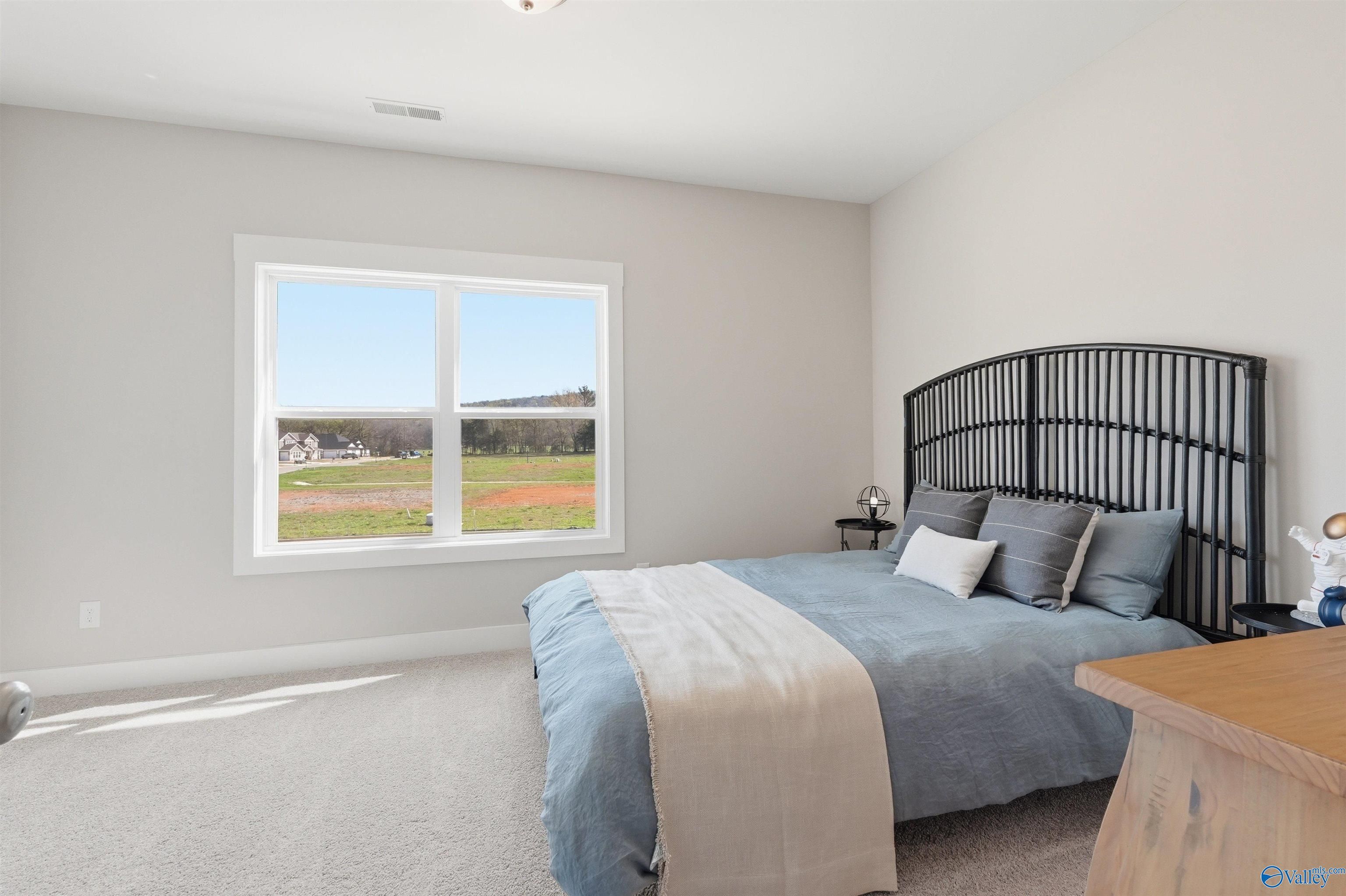 Cozy bedroom with black metal headboard, blue bedding, and scenic field view through large window in Evermore Homes The Oxford B, Owens Cross Roads