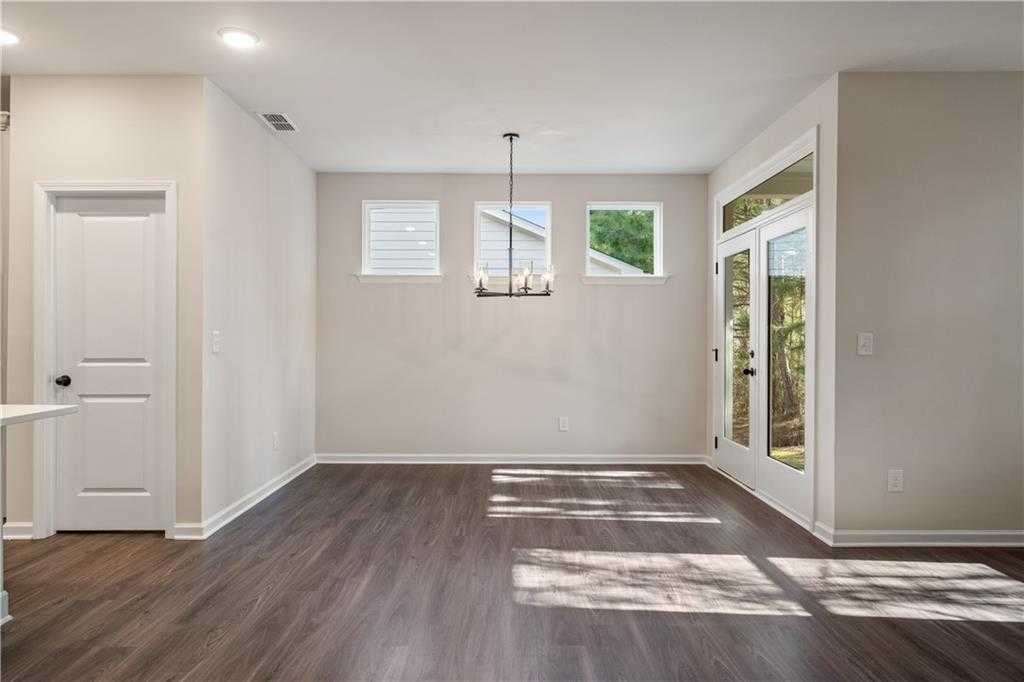 Bright dining room with chandelier, French doors to wooded view, hardwood floors in The Daphne B, Loganville GA
