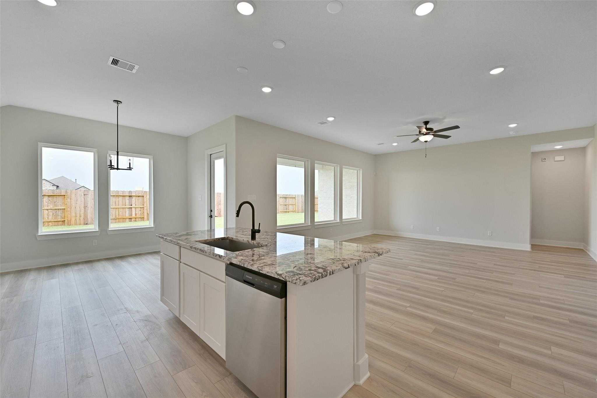 Open-concept kitchen with granite island, stainless dishwasher, and large windows overlooking backyard in Davidson Homes The Edward C, Texas City