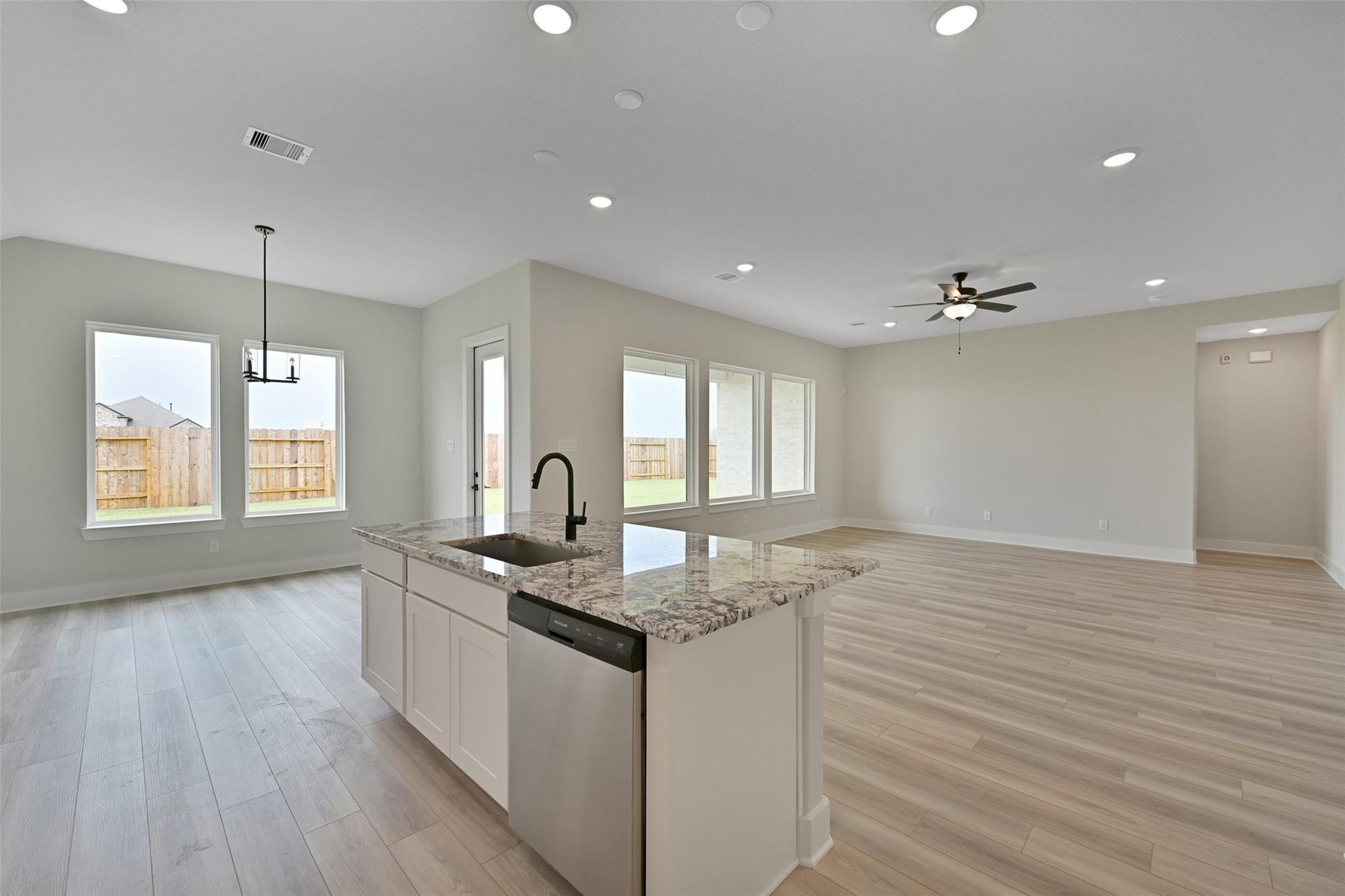 Open-concept kitchen with granite island sink, white cabinets, and backyard views in Davidson Homes The Edward C, Lago Mar, Texas