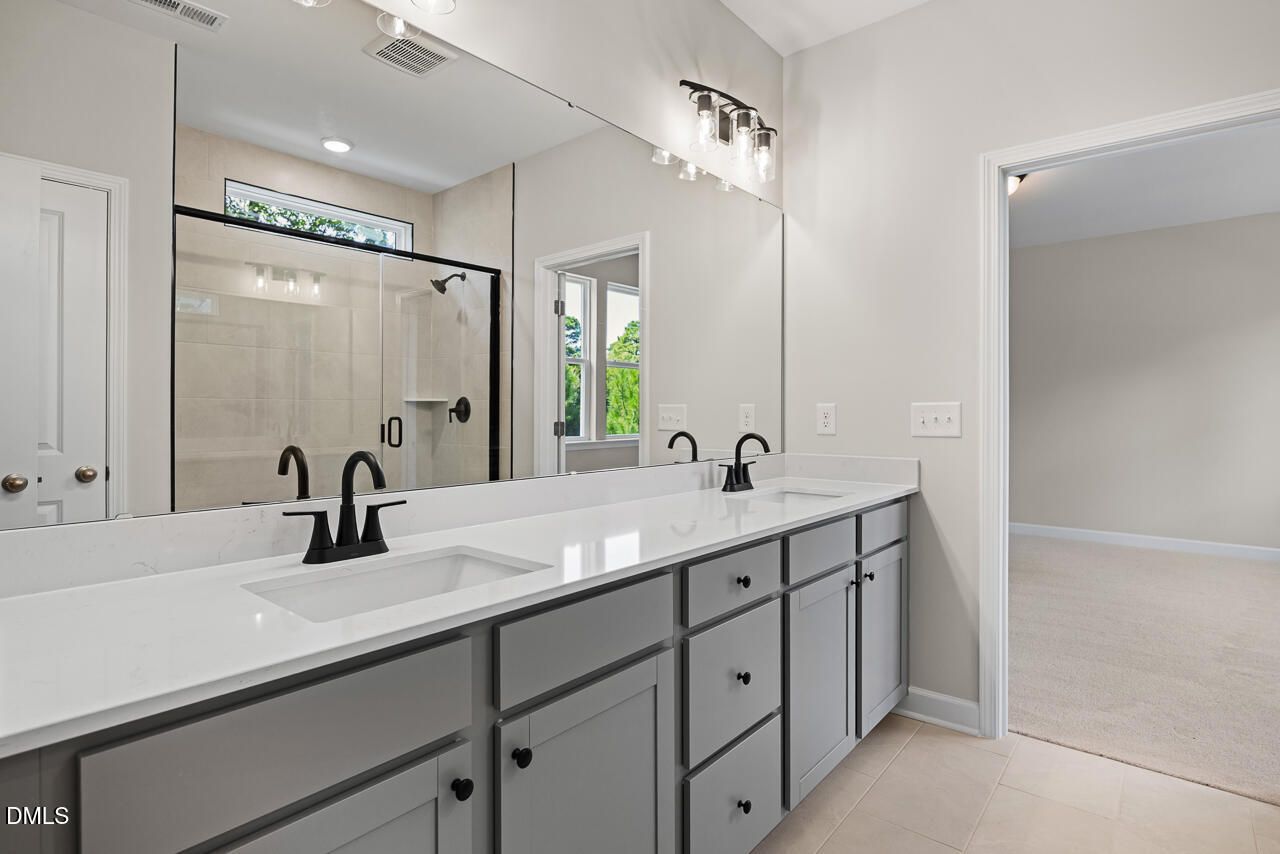 Modern dual-vanity bathroom with gray cabinets and glass-enclosed shower in The Chestnut floor plan, Aberdeen, NC.